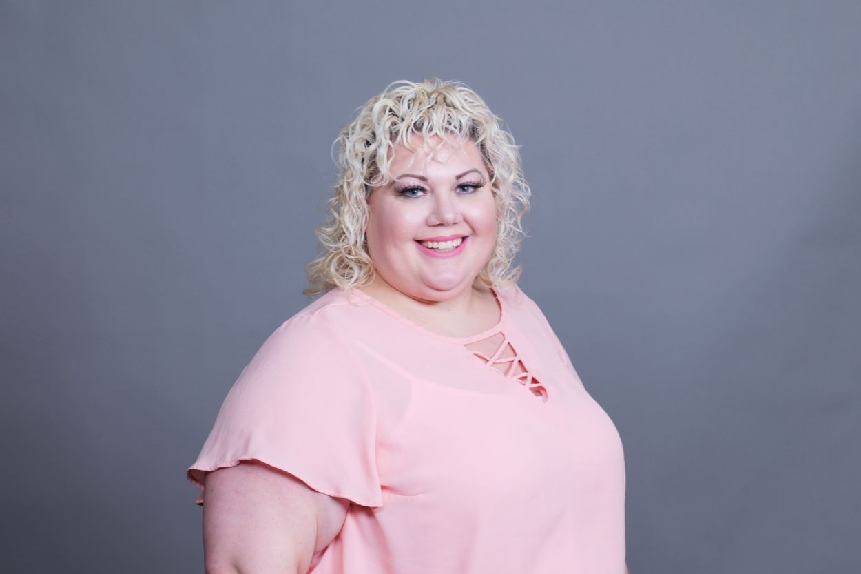 Smiling person in a light pink blouse against a gray studio backdrop