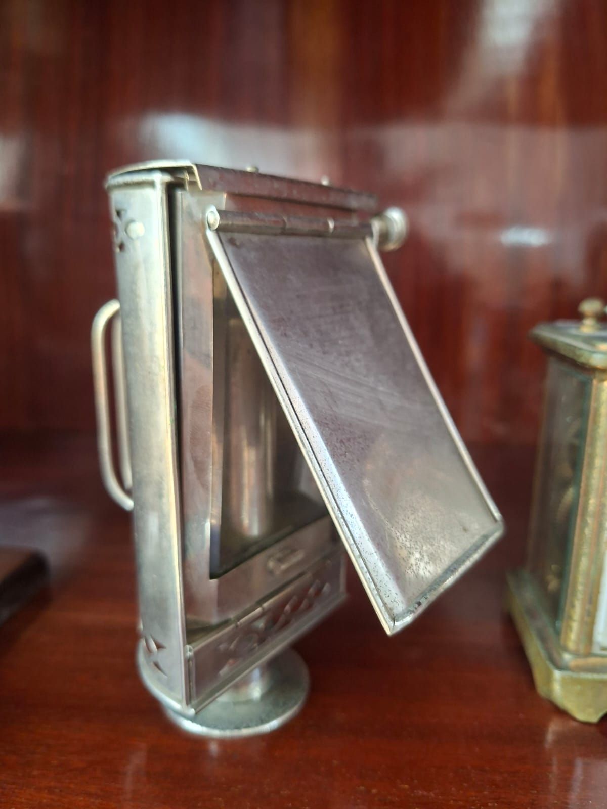 Una lampada vintage rettangolare in metallo color argento, con manico e pannello frontale aperto e incernierato, è posizionata su una superficie di legno.