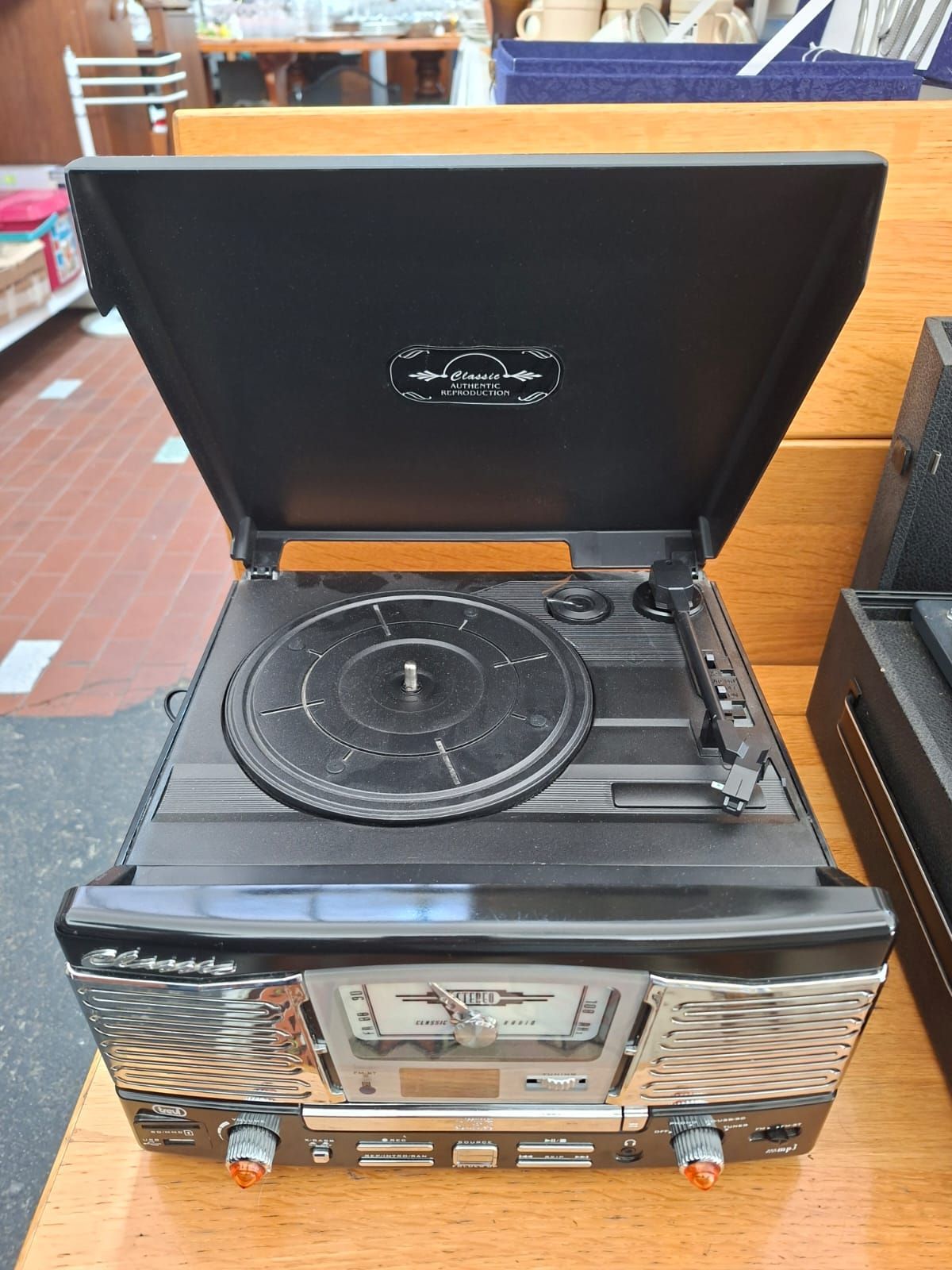Un giradischi e una radio a console in stile retrò di colore nero, con il coperchio aperto, appoggiati su una superficie di legno.