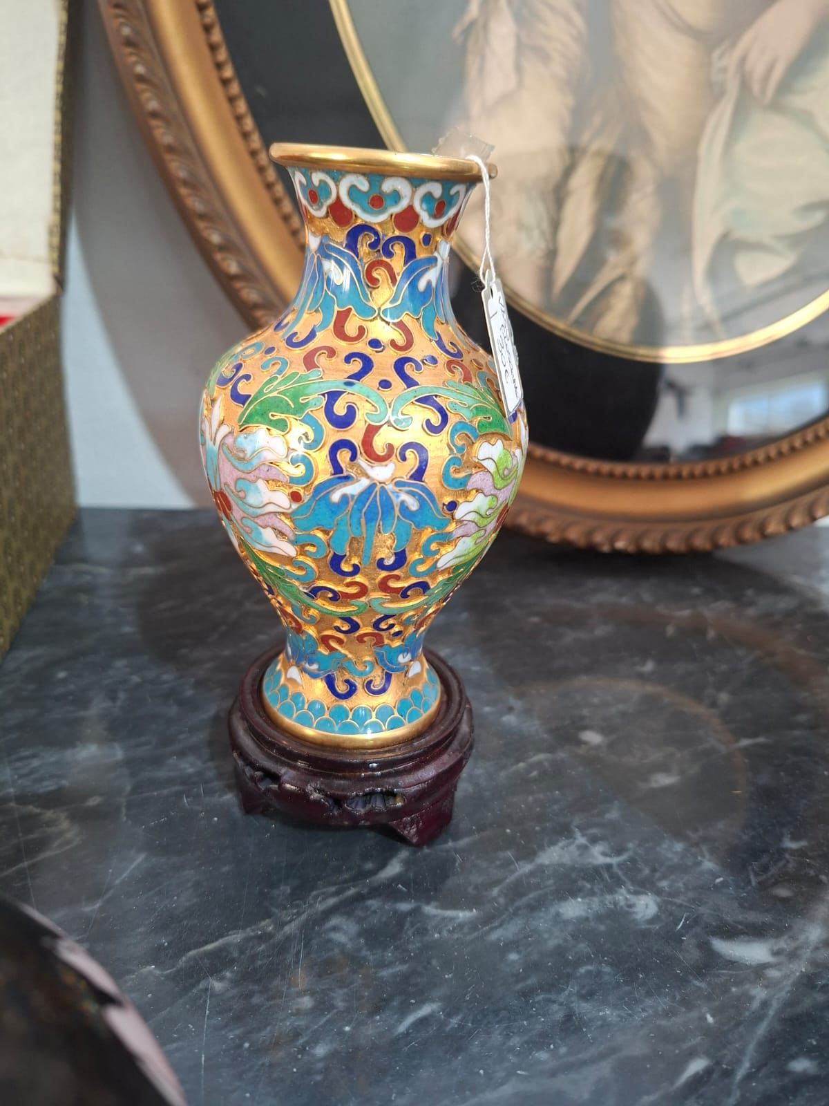 Un piccolo vaso cloisonné colorato con filigrana dorata e motivi floreali, esposto su un supporto di legno.