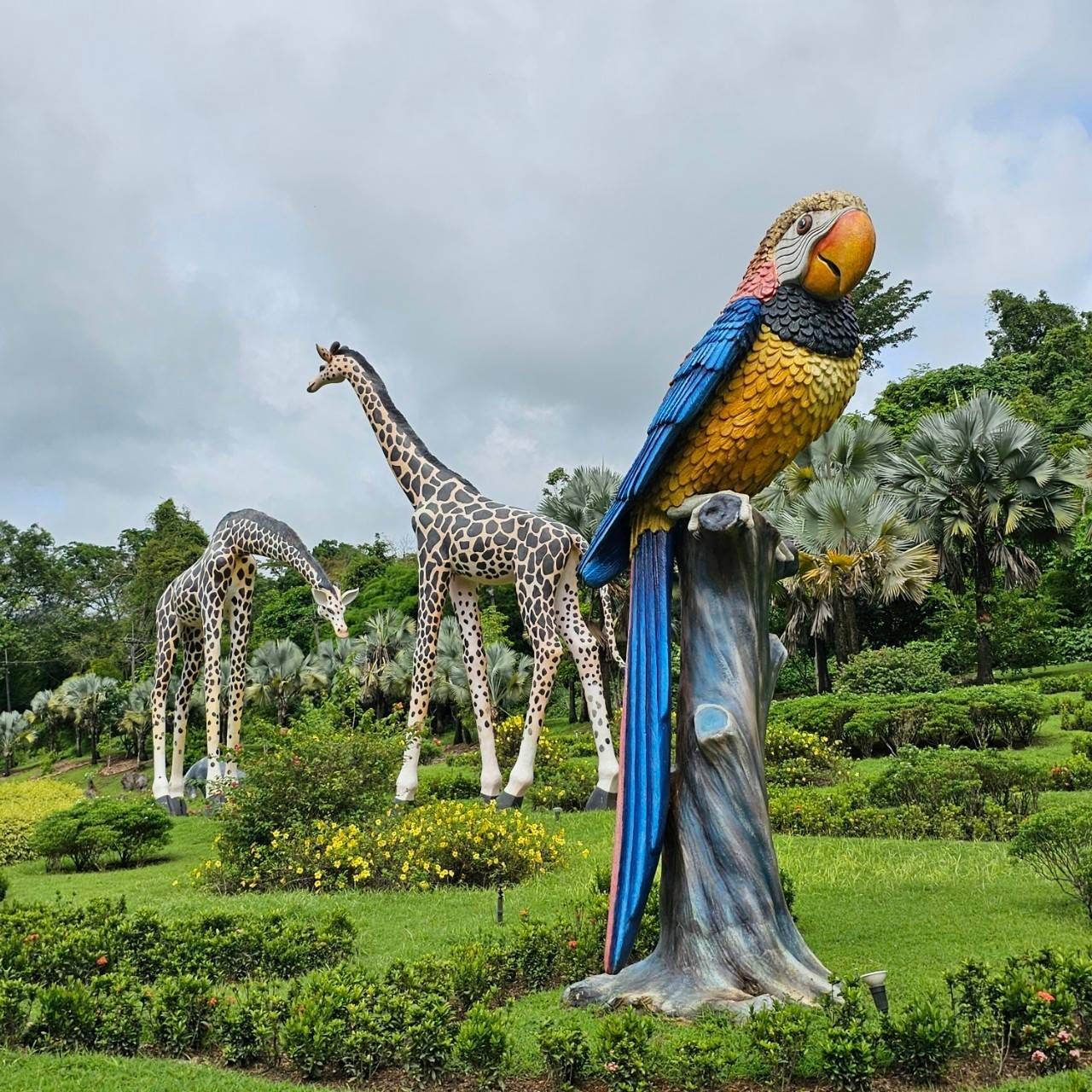 A statue of a parrot sitting on a tree stump with giraffes in the background