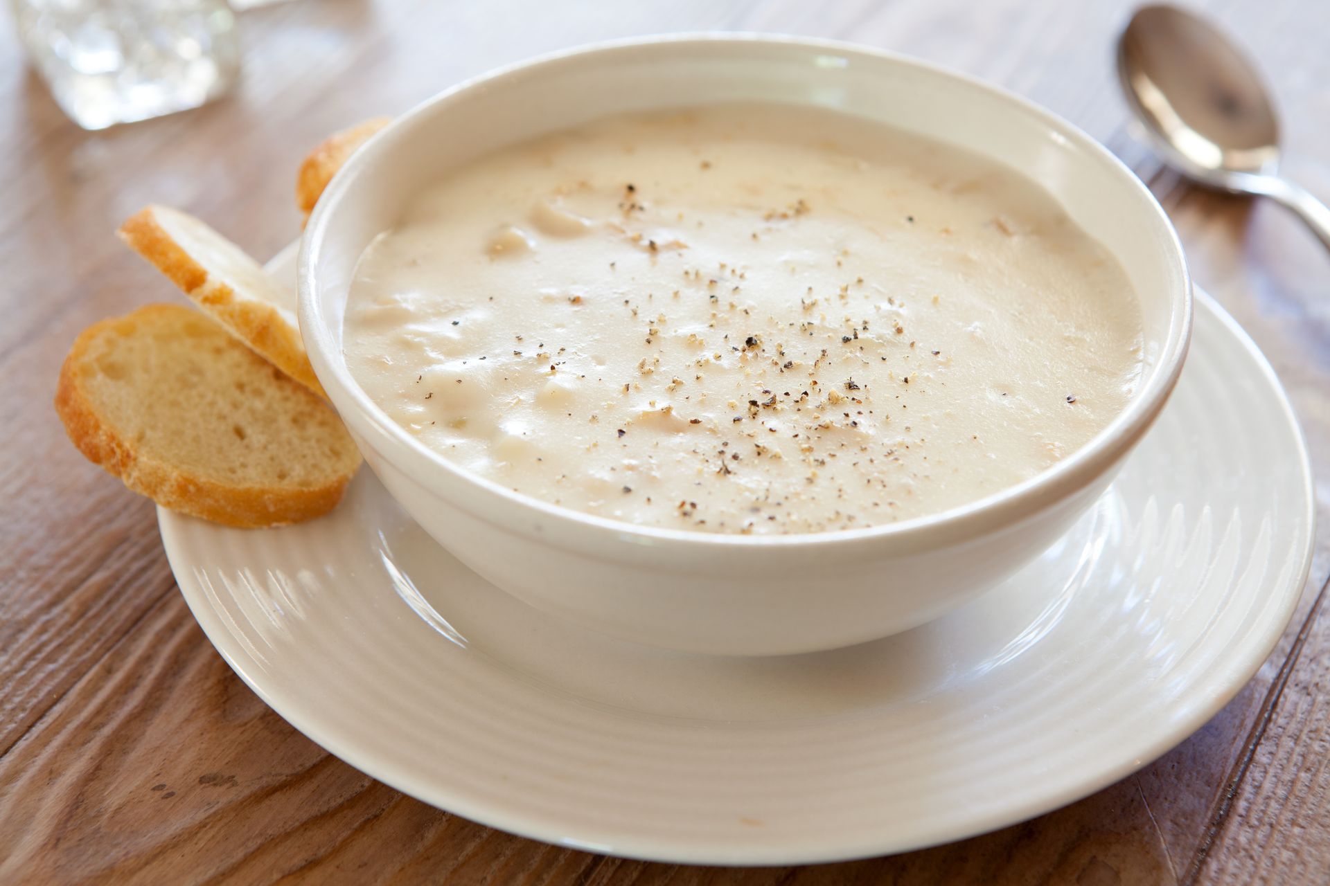 A bowl of soup with crackers and a spoon on a plate.