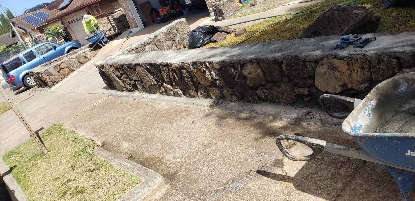 Residential sidewalk with a lava rock retaining wall and blue wheelbarrow in the foreground