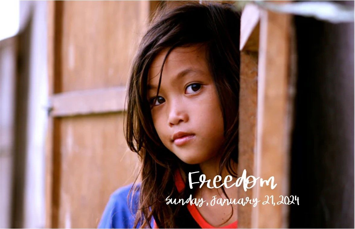 Young child peeking through a wooden window, wearing a blue shirt, with the word “Freedom” overlaid.