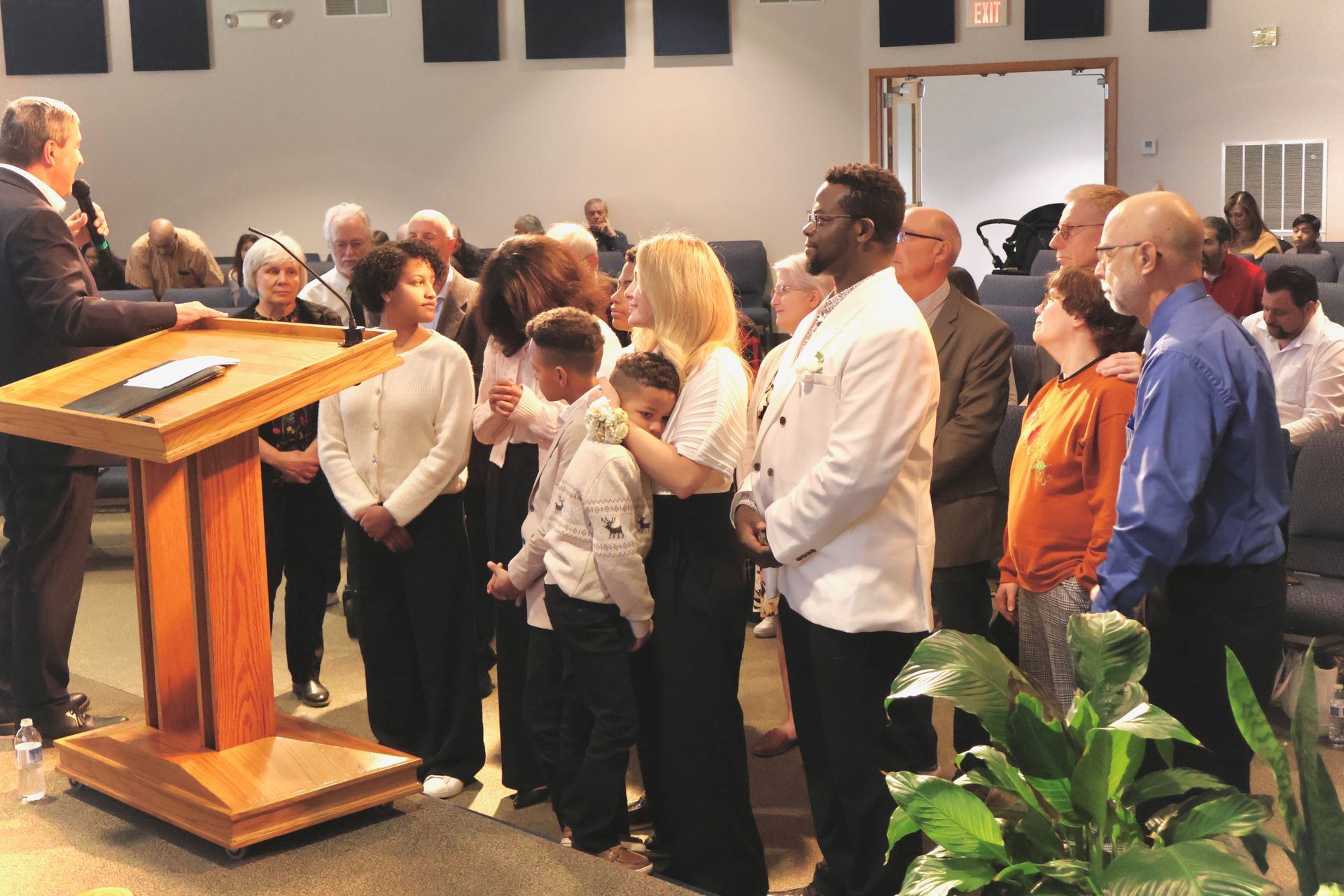 People standing in a church near a wooden lectern, listening to a speaker at the front