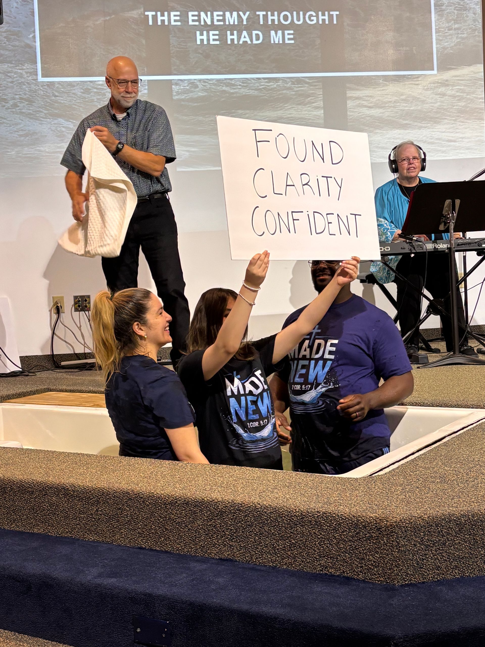 People speaking on stage while two others hold a protest sign in a baptismal pool