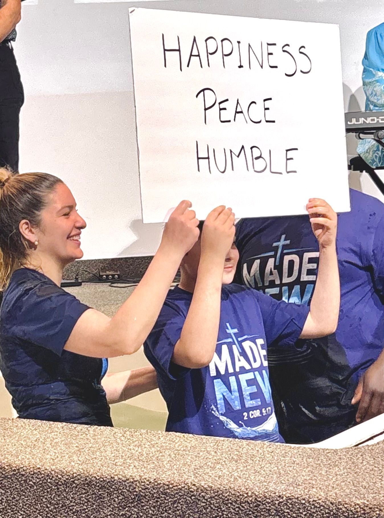 People holding a sign that reads “HAPPINESS PEACE HUMBLE” at a rally
