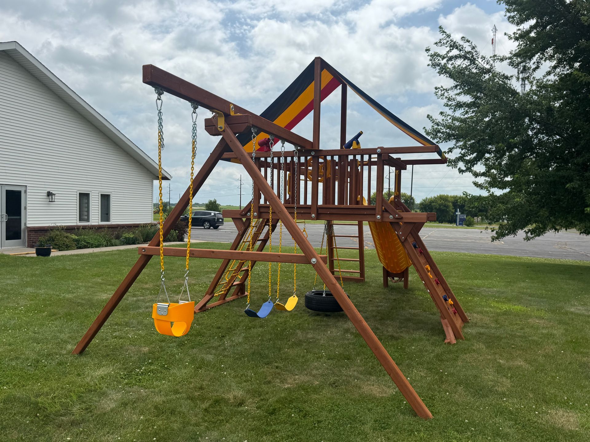 Wooden backyard playset with swings and slide on a grassy lawn beside a white house