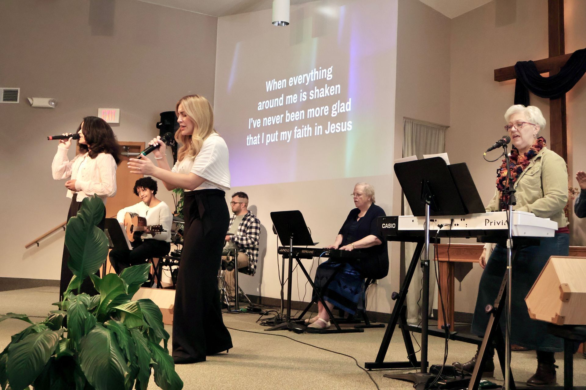 Worship band performing on a church stage with singers, keyboard, and projected lyrics behind them