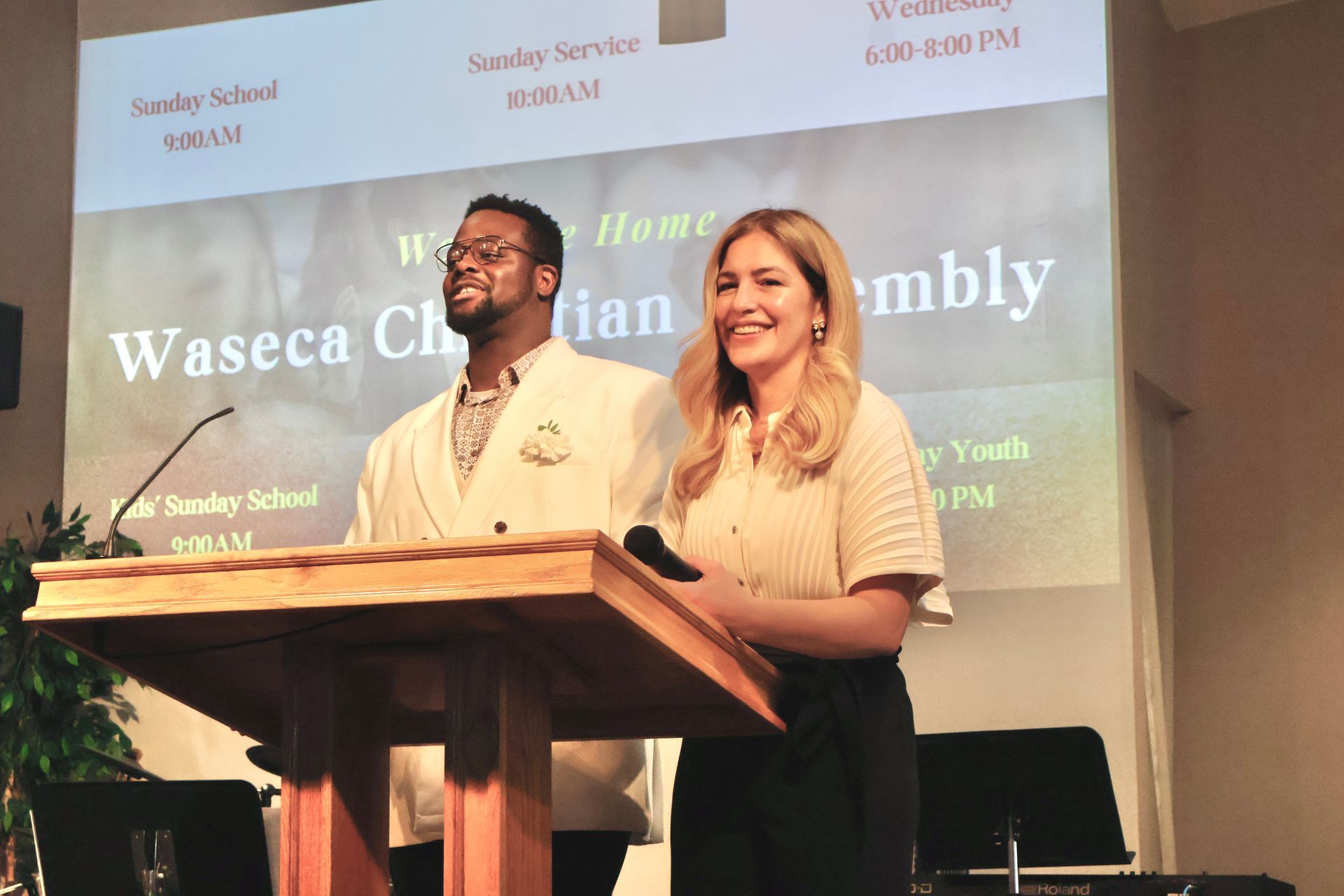 Two smiling speakers stand behind a wooden podium on a church stage with a banner backdrop