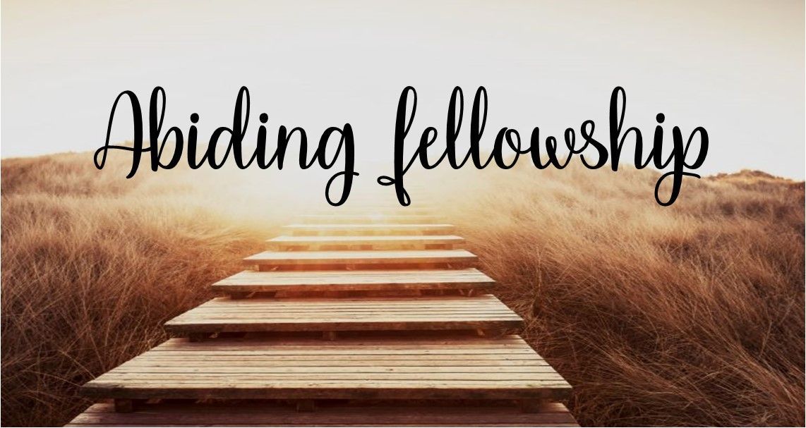 A wooden bridge leading to a field with the words abiding fellowship written on it.