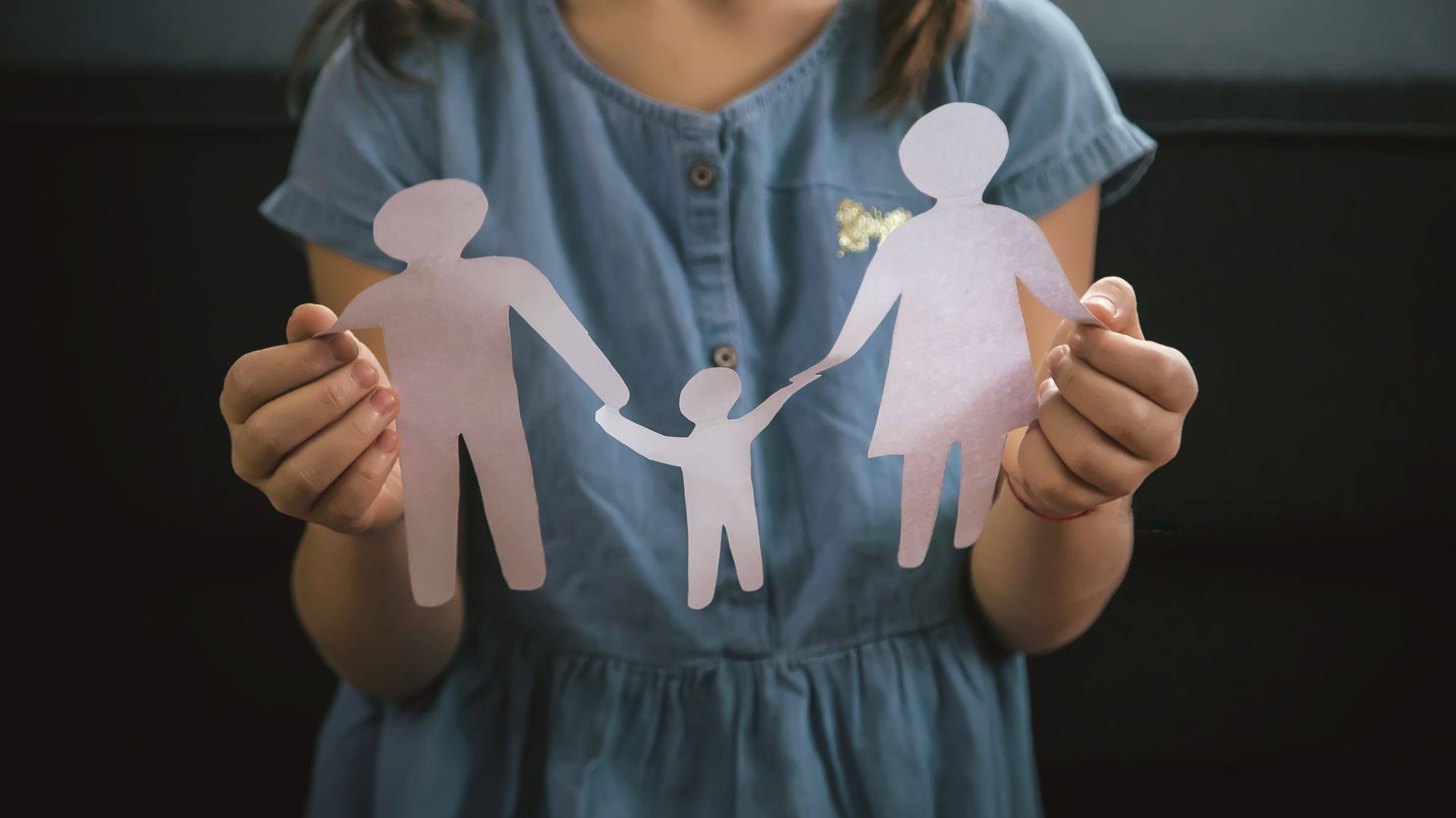 A child holding paper cutouts of a family, against a dark background.