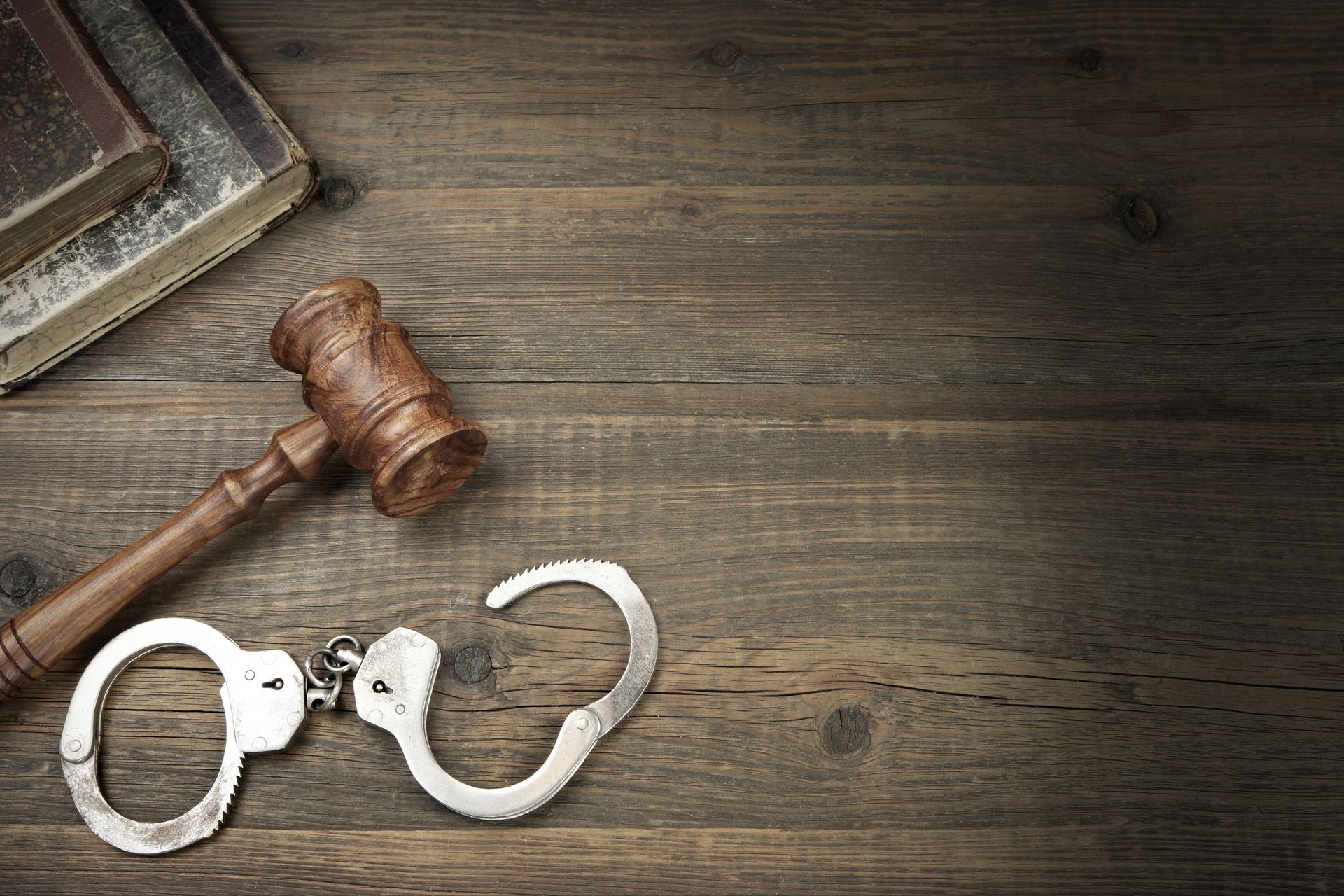 Wooden gavel, handcuffs, and books on a wooden surface, suggesting legal or justice themes.