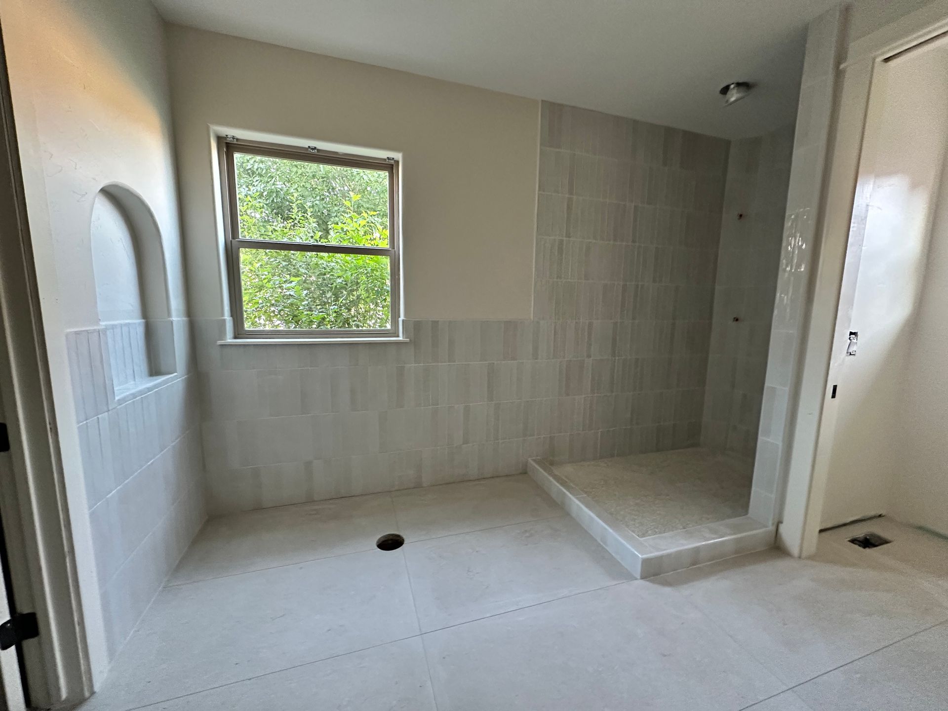 Empty tiled bathroom with a walk-in shower and window letting in natural light.