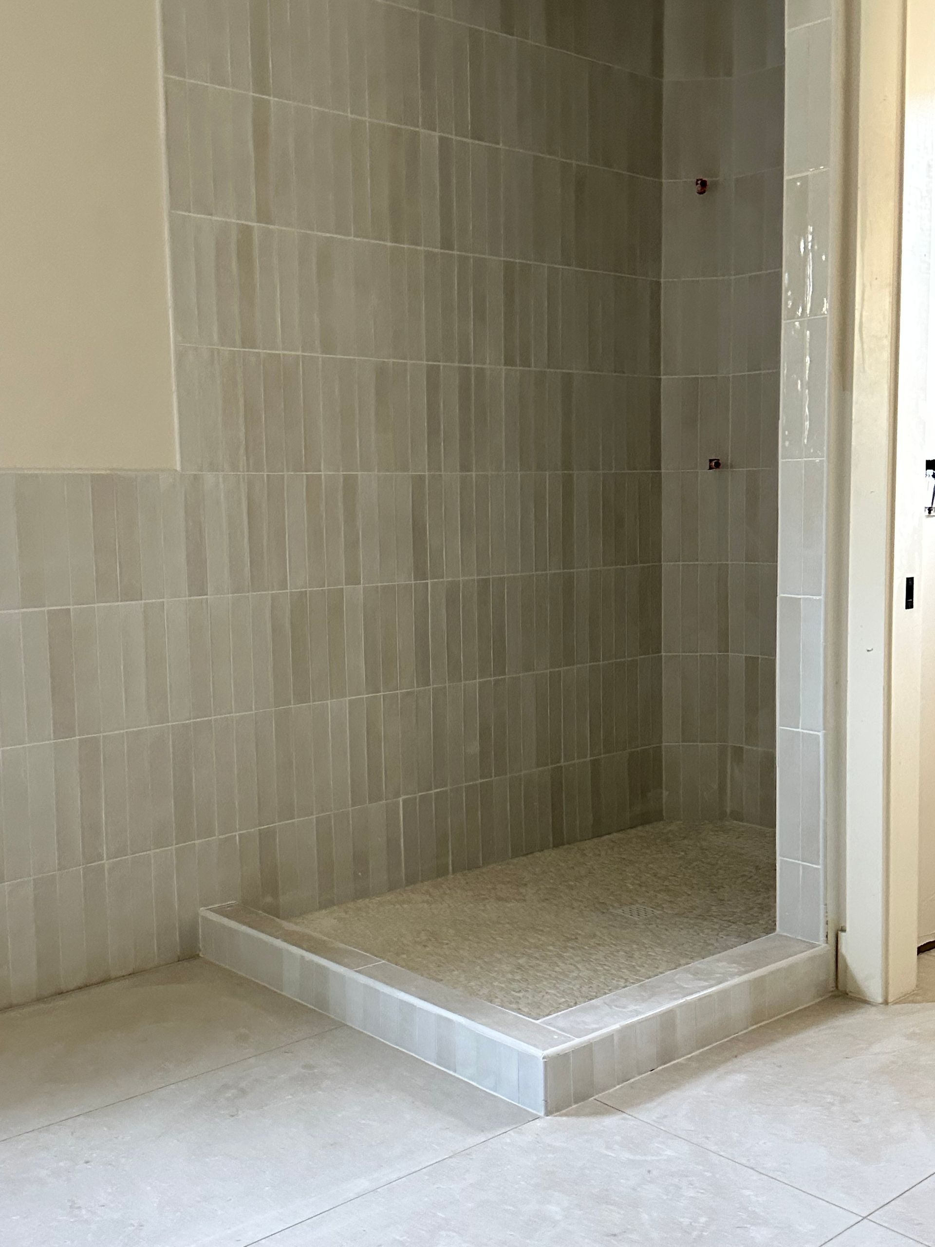 Empty tiled shower stall with a raised step and white walls
