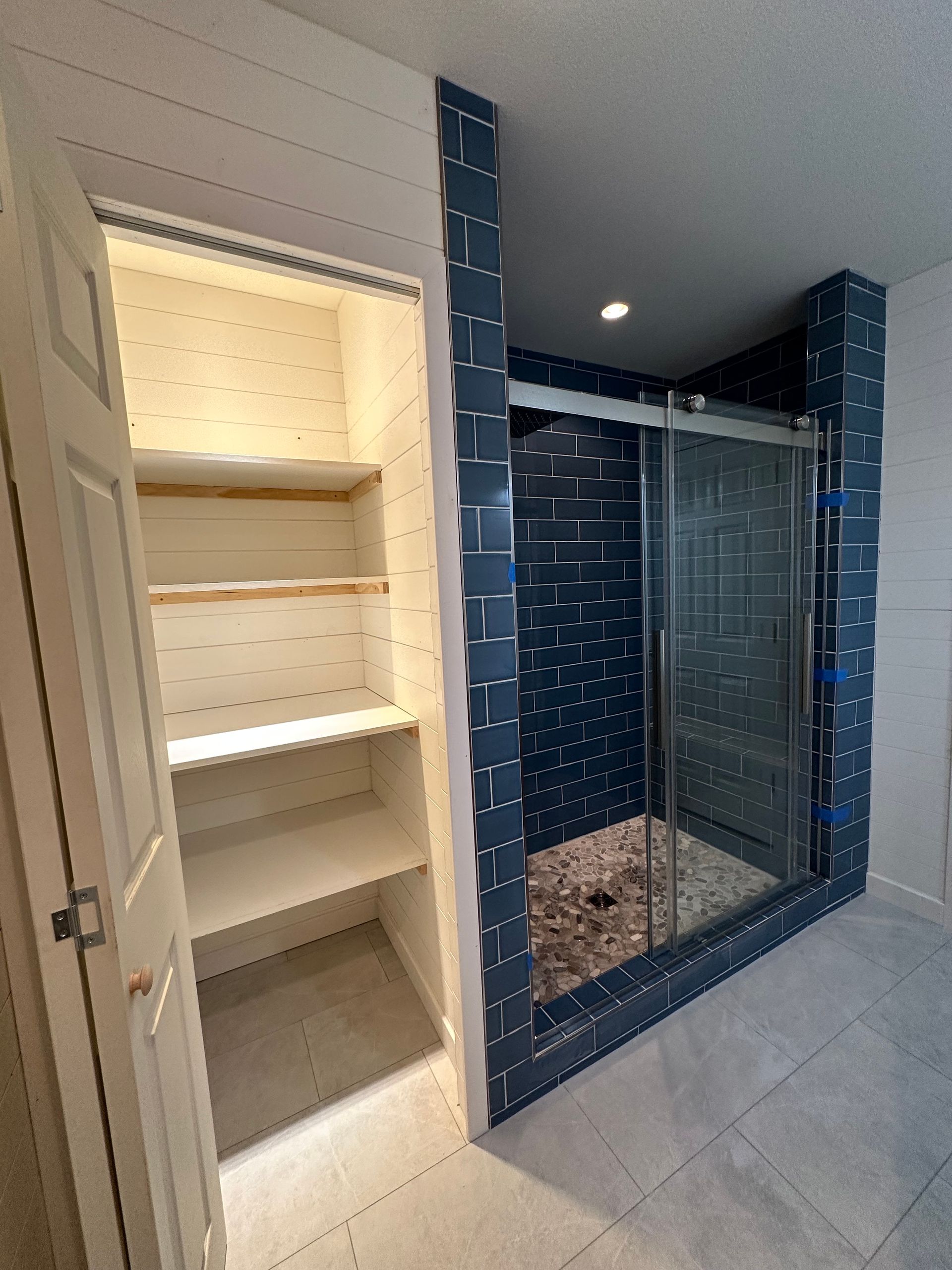 Built-in closet beside a blue-tiled glass shower in a modern bathroom.