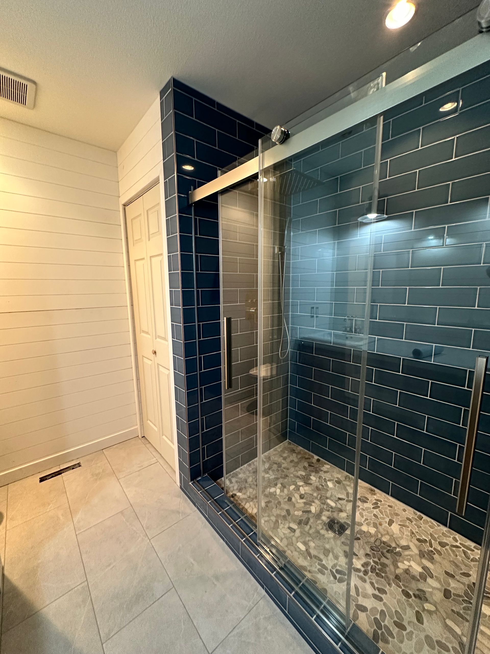 Bathroom with a glass-enclosed shower, black tile accents, and white walls and floor.