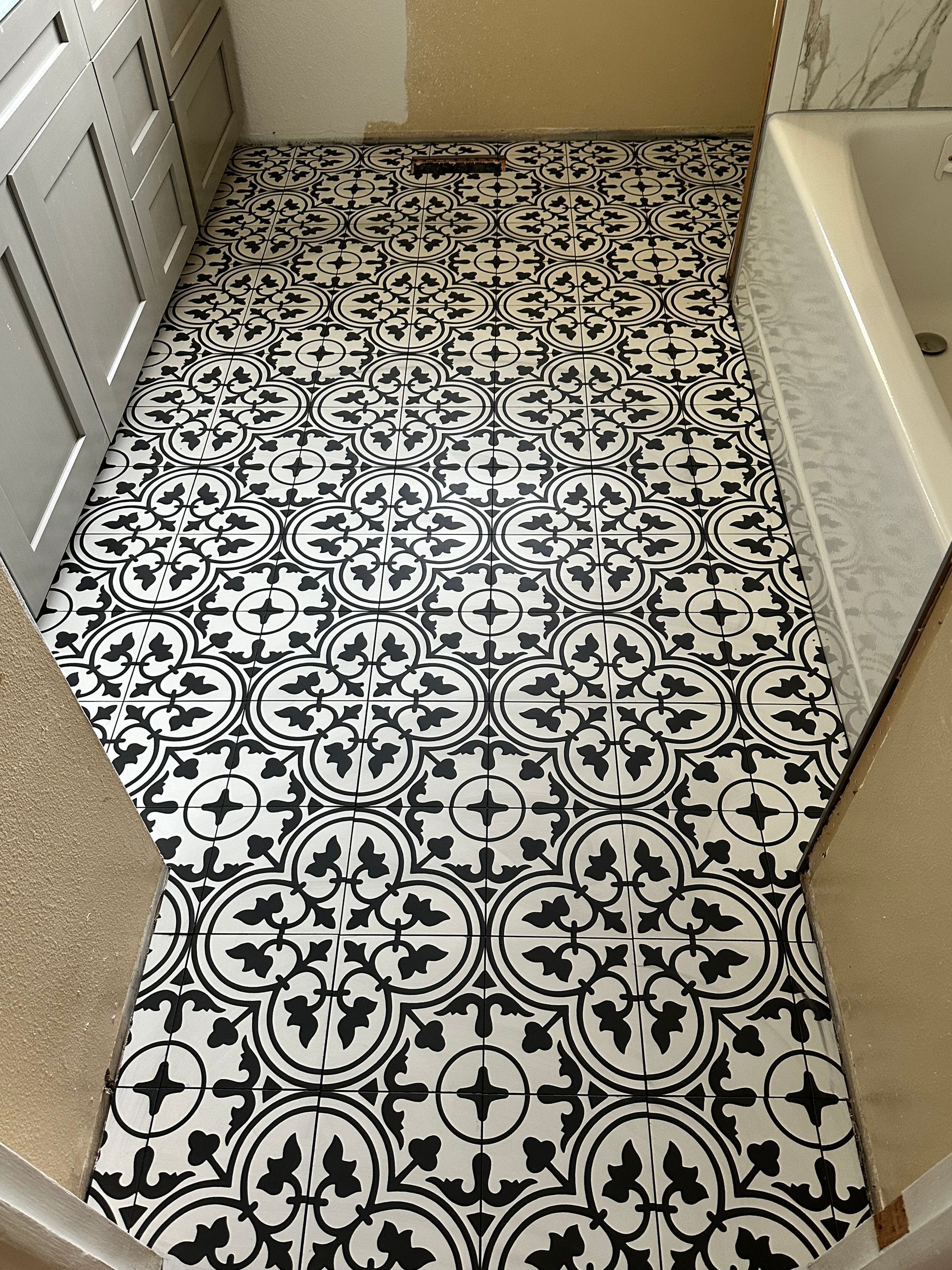 Black-and-white patterned floor tiles in a narrow hallway beside a bathtub and cabinets