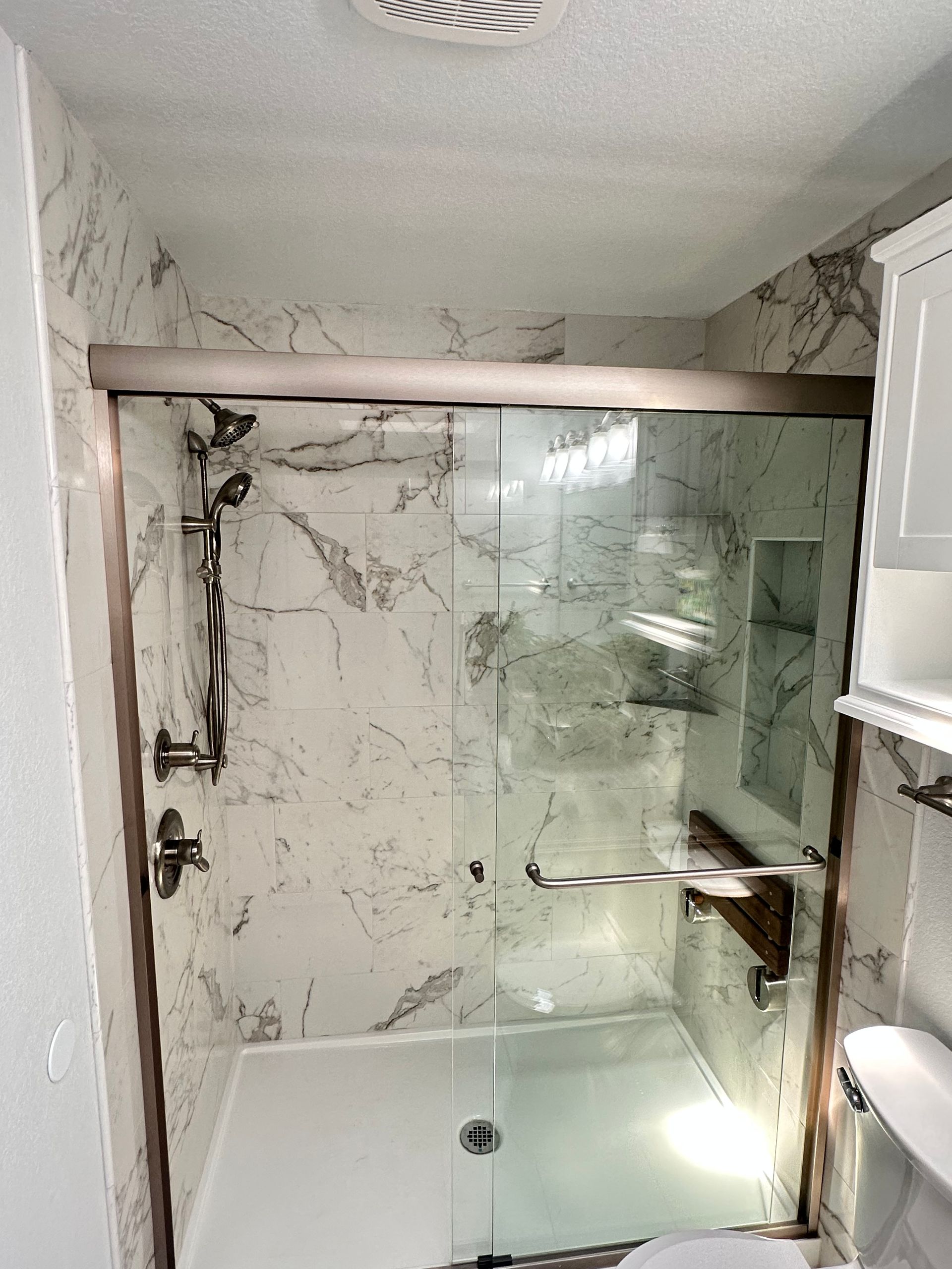 Small tiled bathroom with a bathtub-shower, glass partition, and a frosted window.