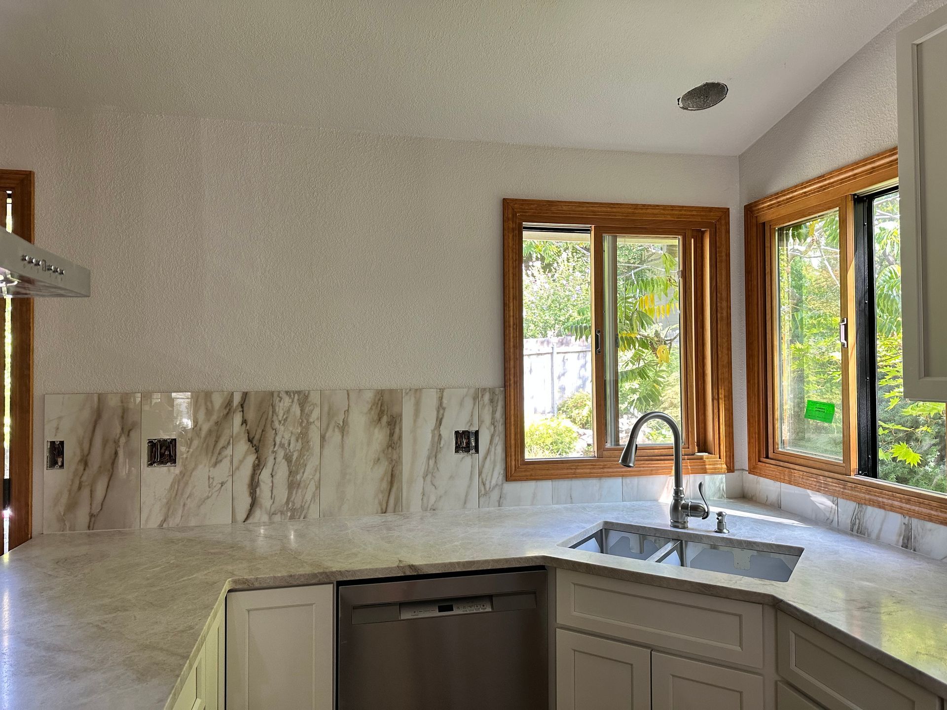 Bright kitchen with marble countertops, stainless sink, and large wood-framed windows overlooking greenery