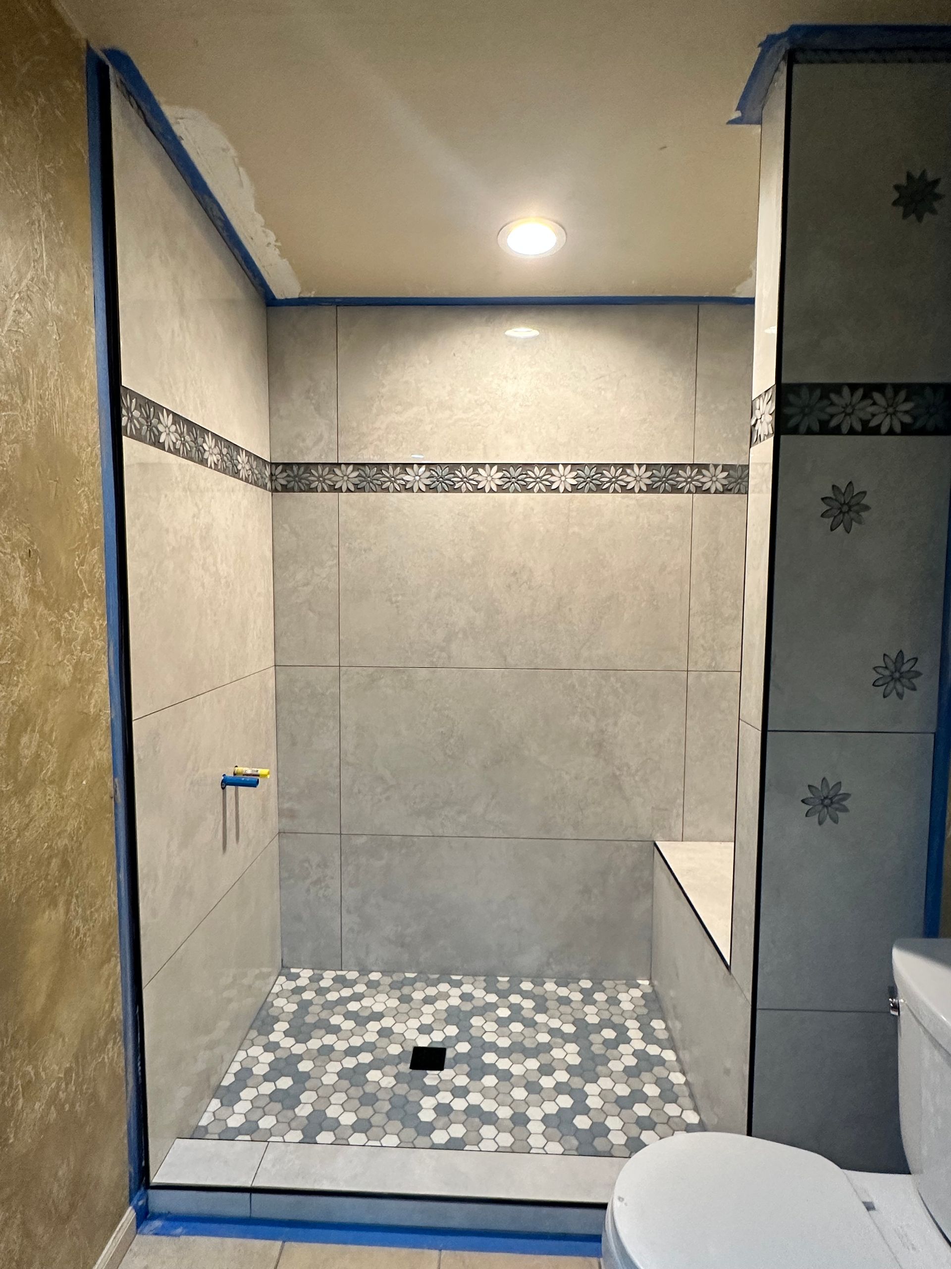 Tiled bathroom shower with blue painter’s tape and a mosaic shower floor under construction