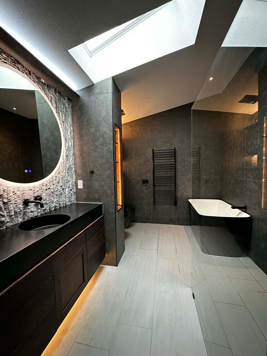 A bathroom with a bathtub , sink , mirror and skylight.