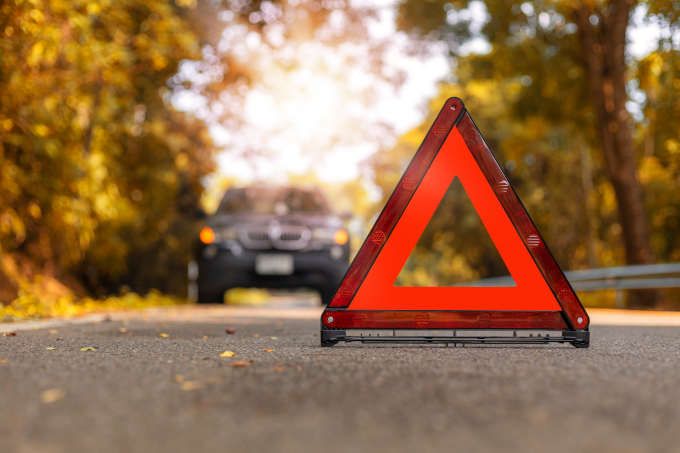 Orange Hazard Road Sign placed on the road, with a car driving away from it in the background.