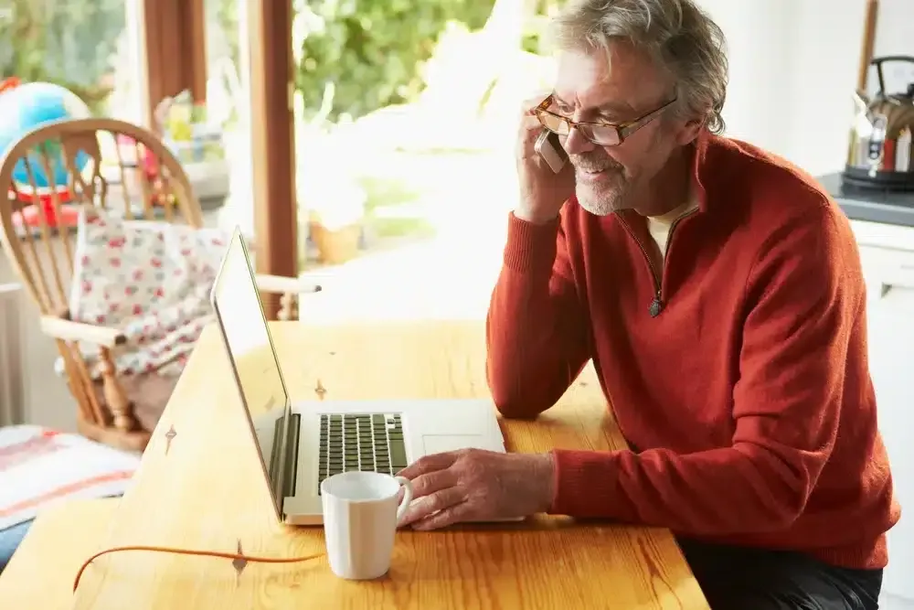 Person in a red sweater using a laptop at a wooden table, looking at the screen with a coffee mug nearby.