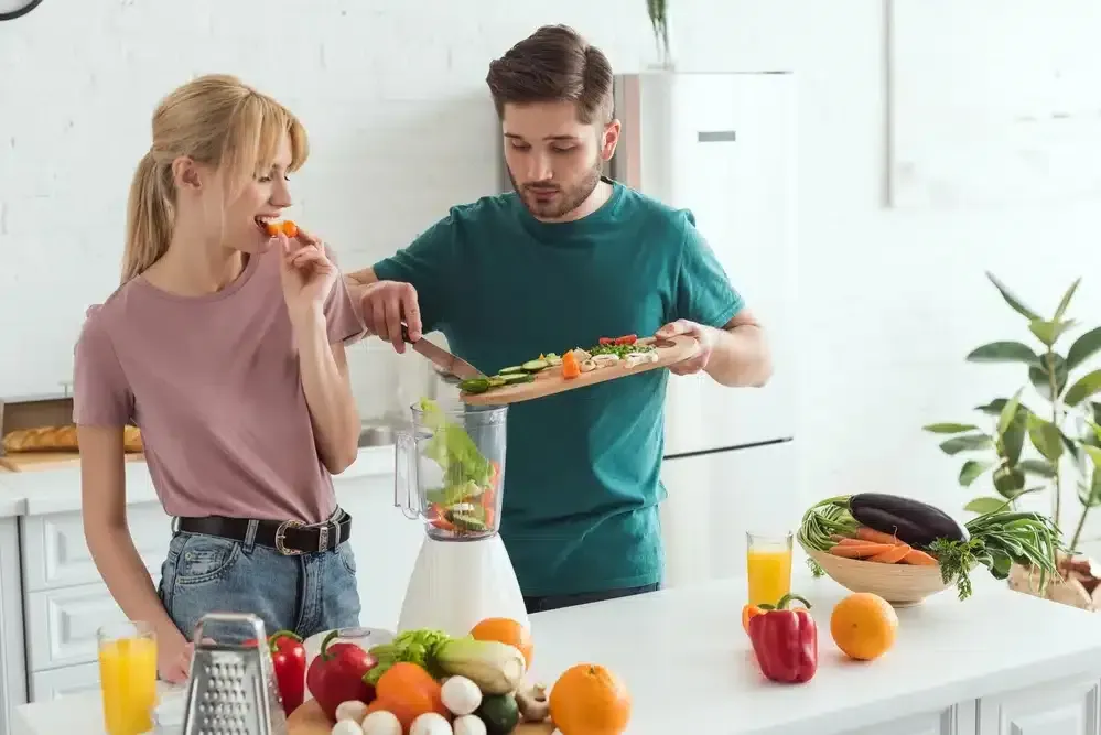 Two people preparing vegetables together in a bright kitchen, with fresh produce on the counter.