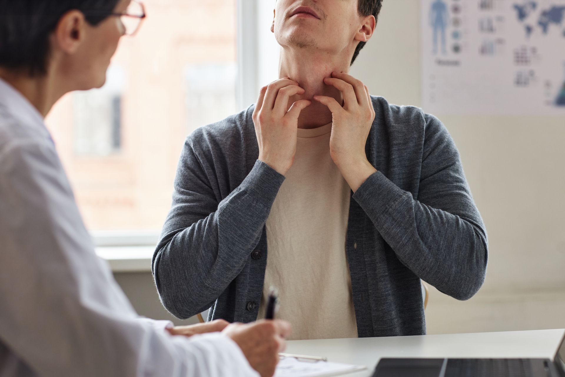 Person touching throat during medical consultation with doctor in office