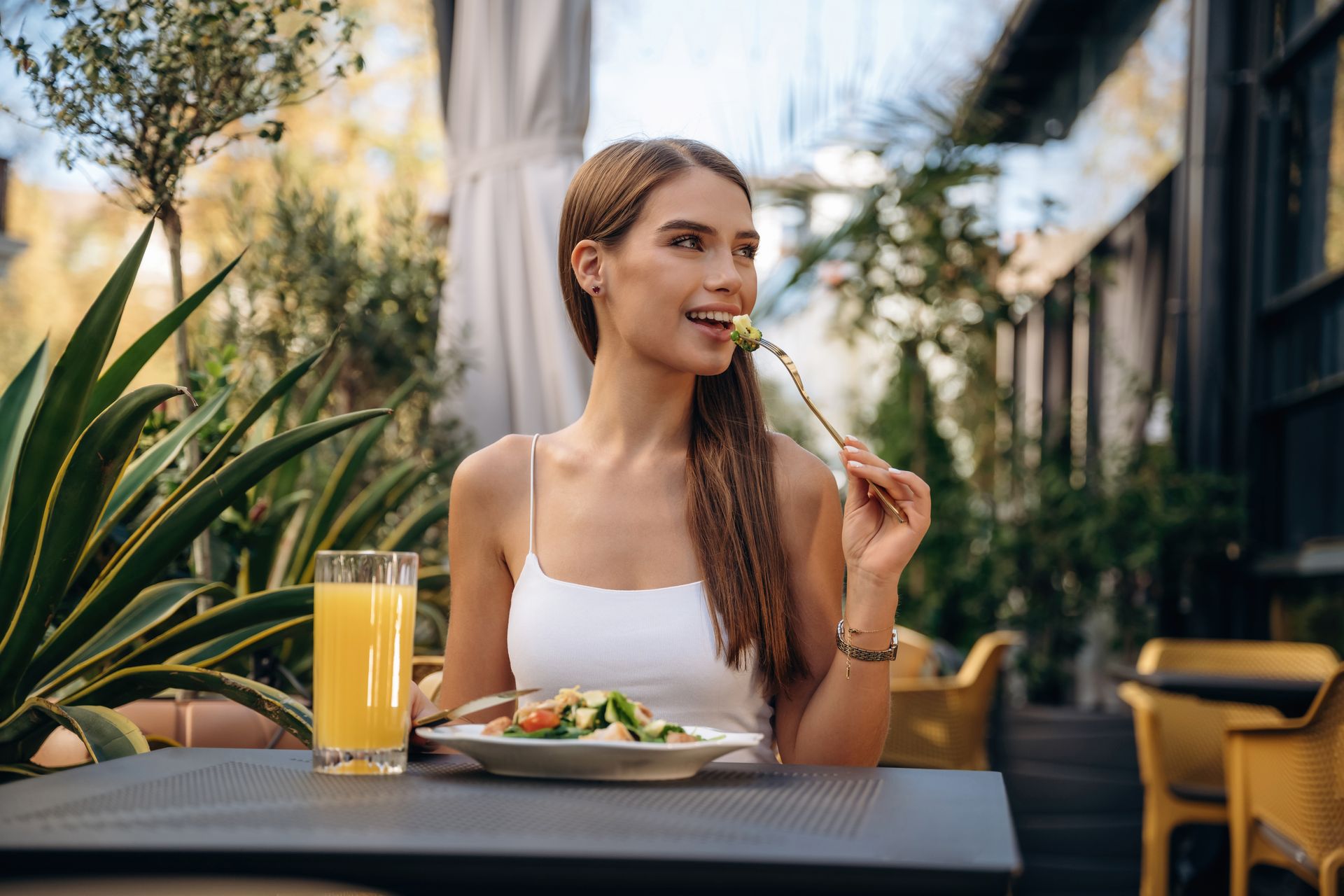 Woman dining outdoors at a cafe, smiling with a drink and plate of food on the table