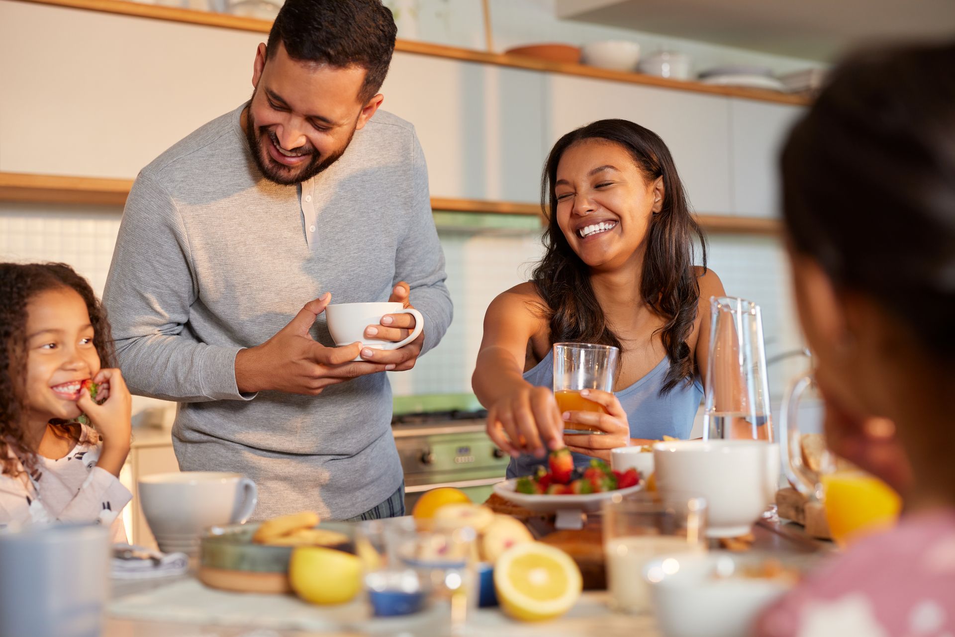 Family sharing a meal at a dining table, smiling and serving food in a bright kitchen