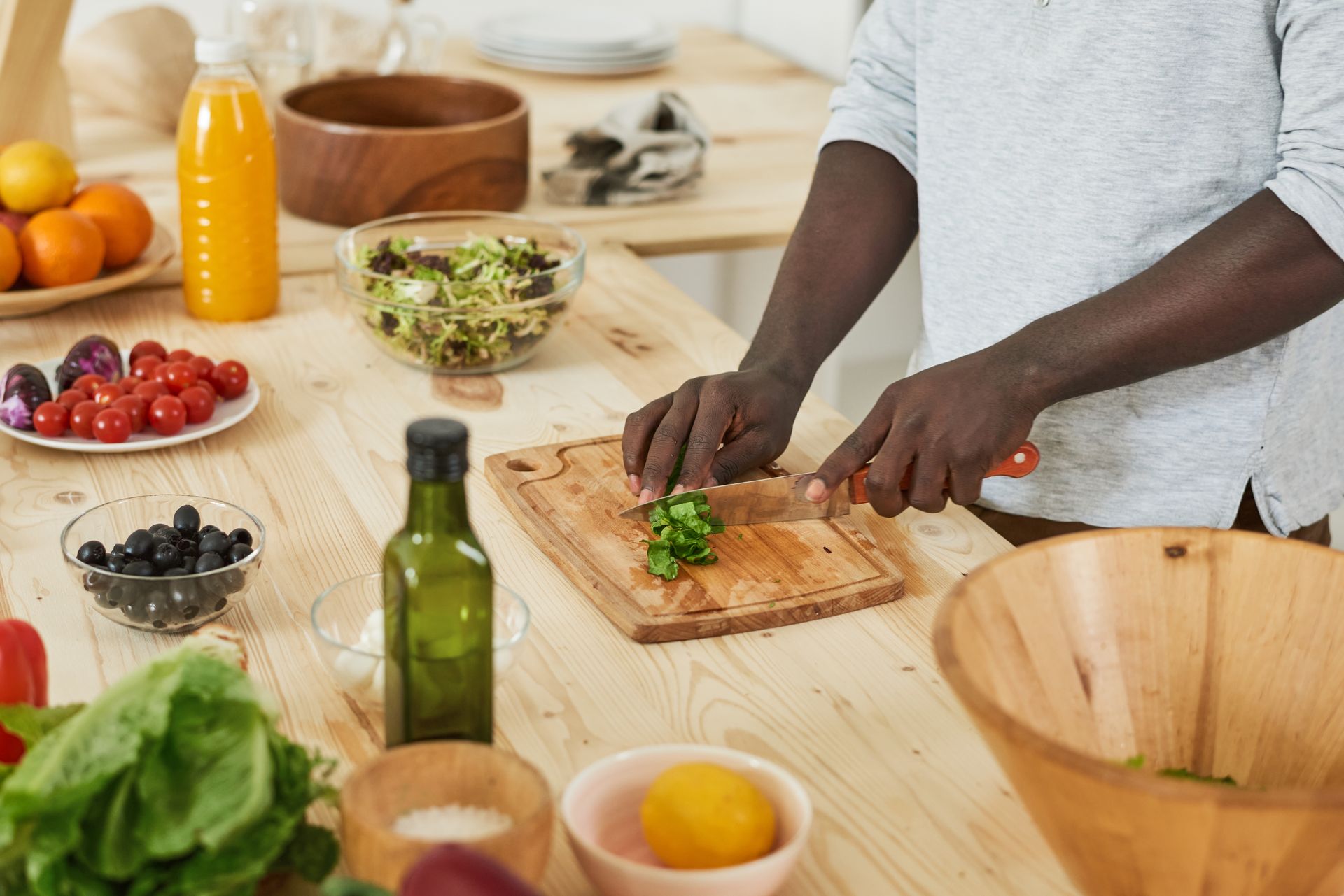 Person chopping herbs on a cutting board in a bright kitchen with fresh produce and bowls nearby