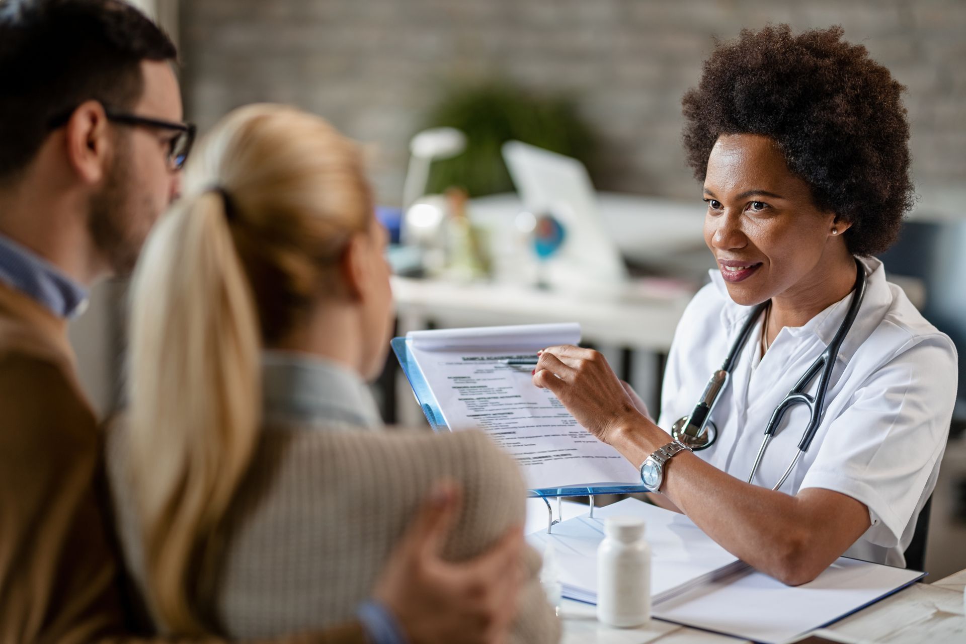 Doctor talking with patients in a bright clinic, holding a clipboard and smiling.