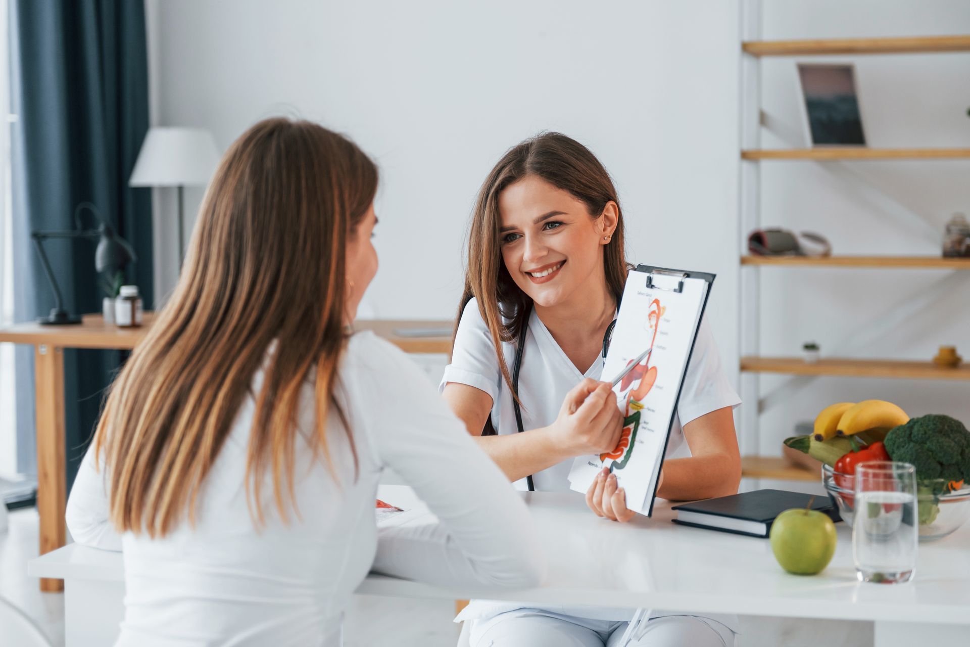 Two people in a bright kitchen discuss a tablet with a fruit bowl on the table.