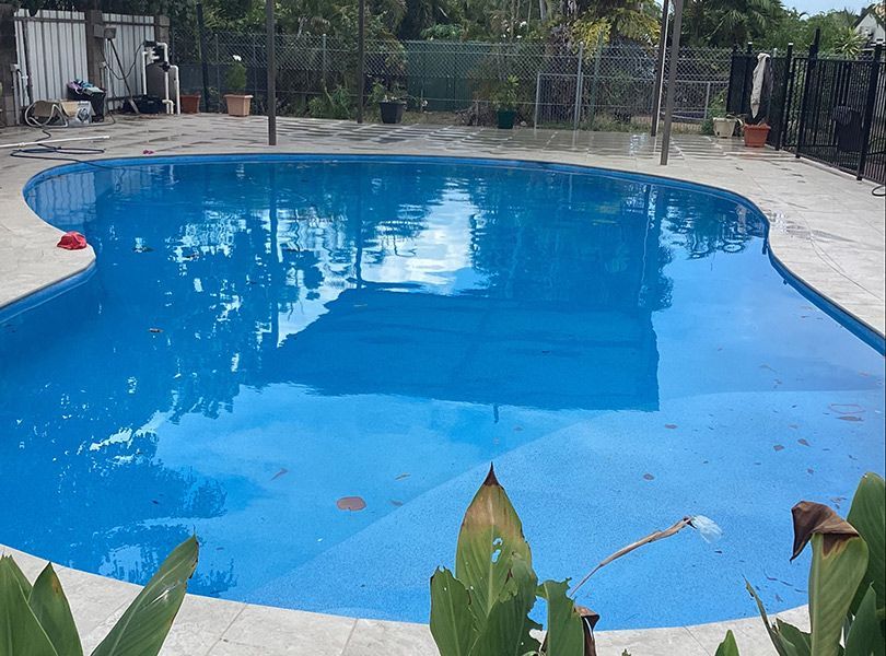 A Large Swimming Pool Is Surrounded by Plants and A Fence — Paving in Darwin River, NT