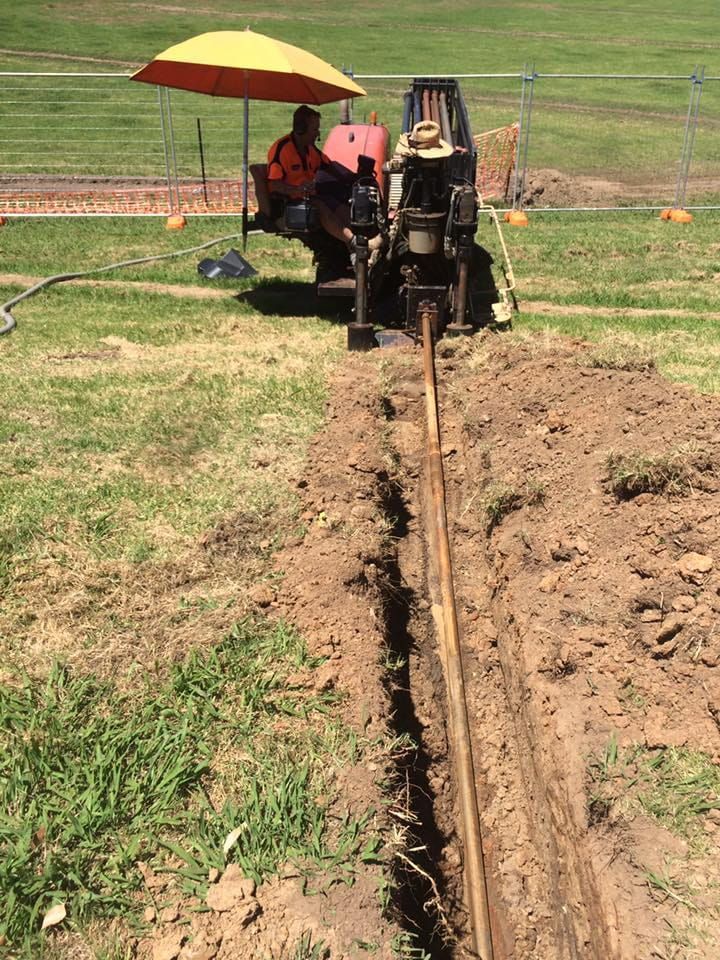 A Man Sits Under An Umbrella Next To A Tractor — Matt Walsh Plumbing in Thurgoona, NSW