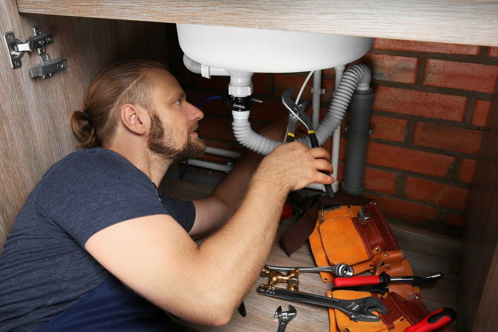 A Man Is Fixing A Sink Under A Cabinet — Matt Walsh Plumbing in Lavington, NSW