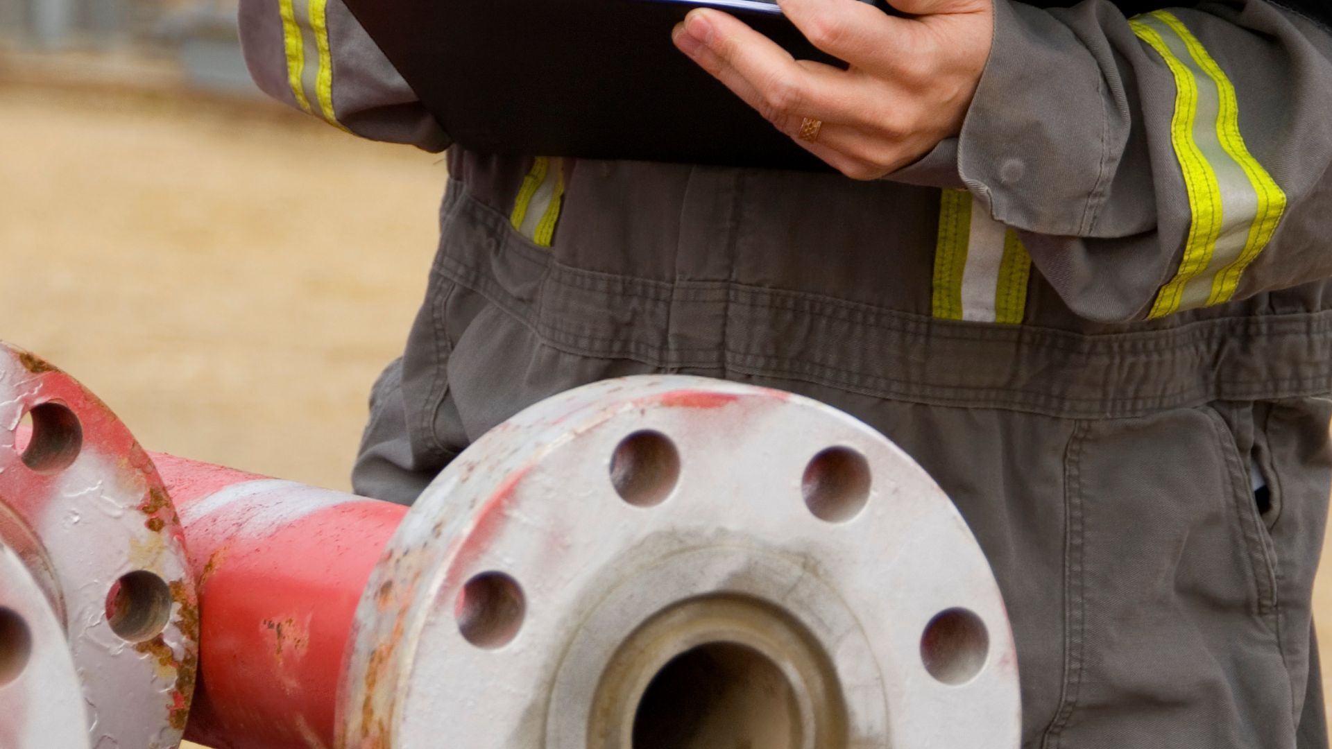 A man is holding a clipboard and looking at a pipe.
