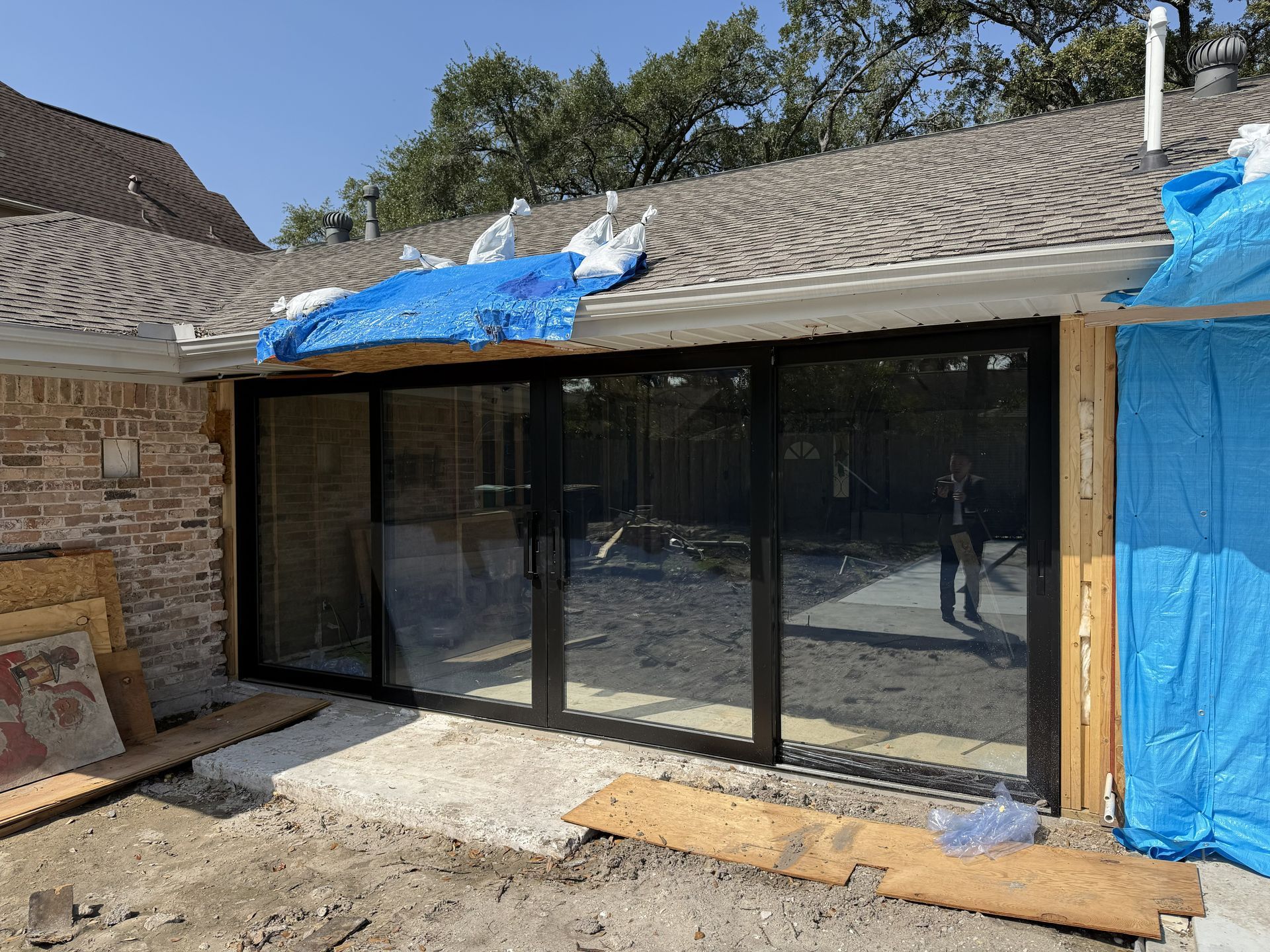 Home exterior with new black sliding glass doors under a tiled roof, blue tarp on the roof and at the right side.