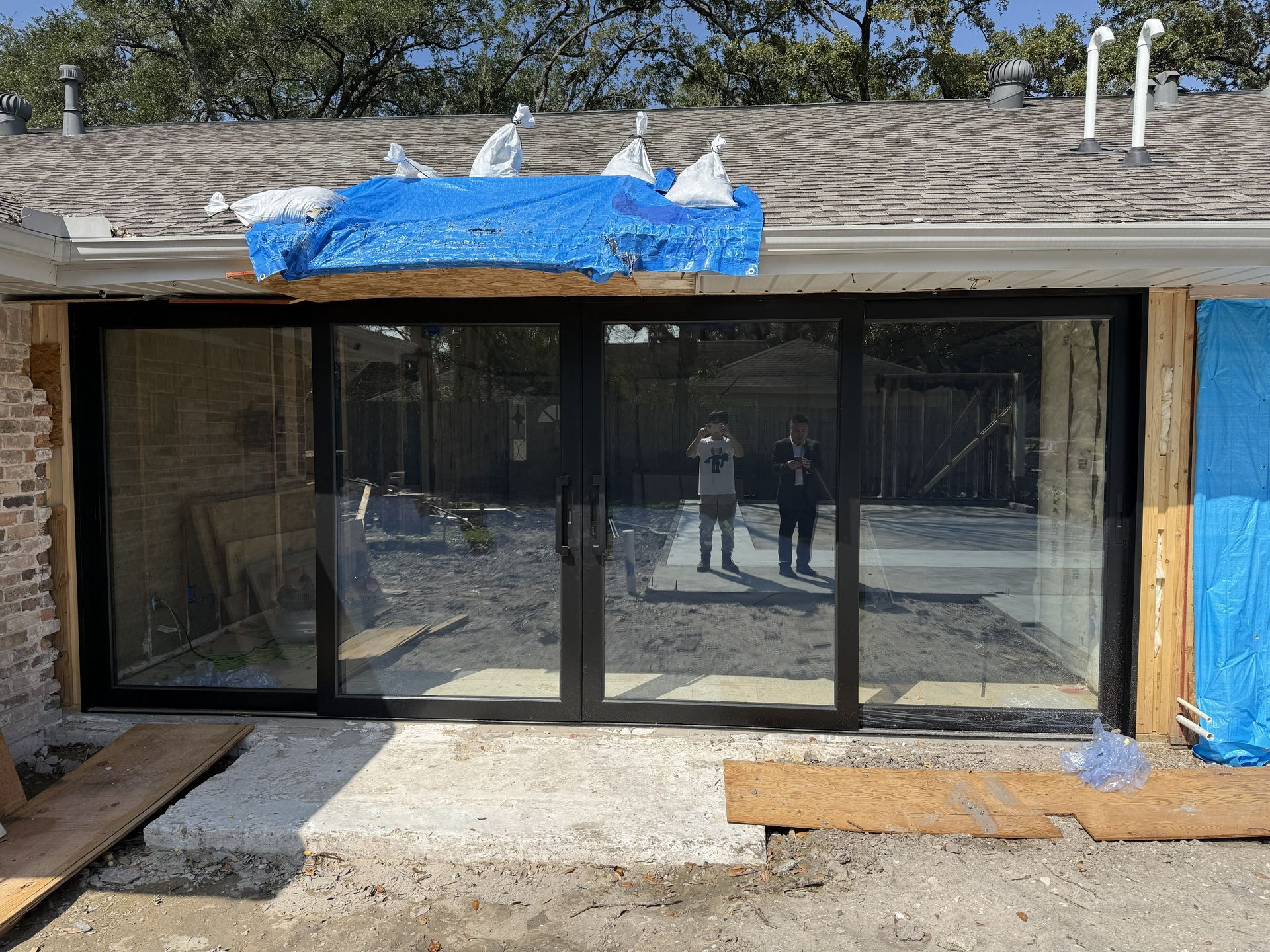 Sliding glass doors under construction with blue tarp on the roof and stone siding around them