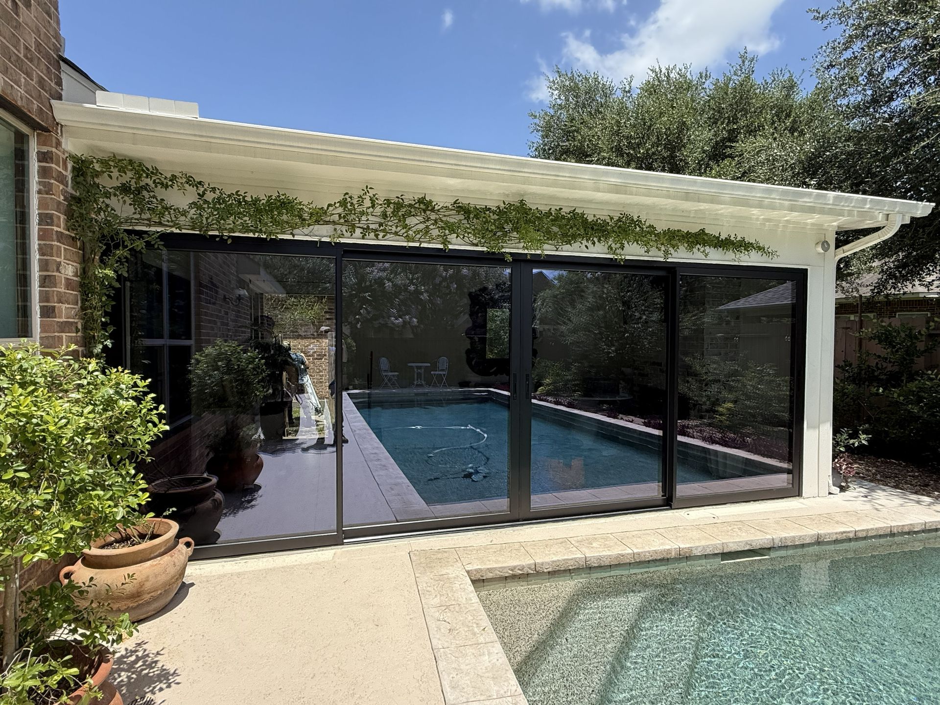 Covered pool patio with glass doors, white pergola roof, and blue swimming pool beside a house