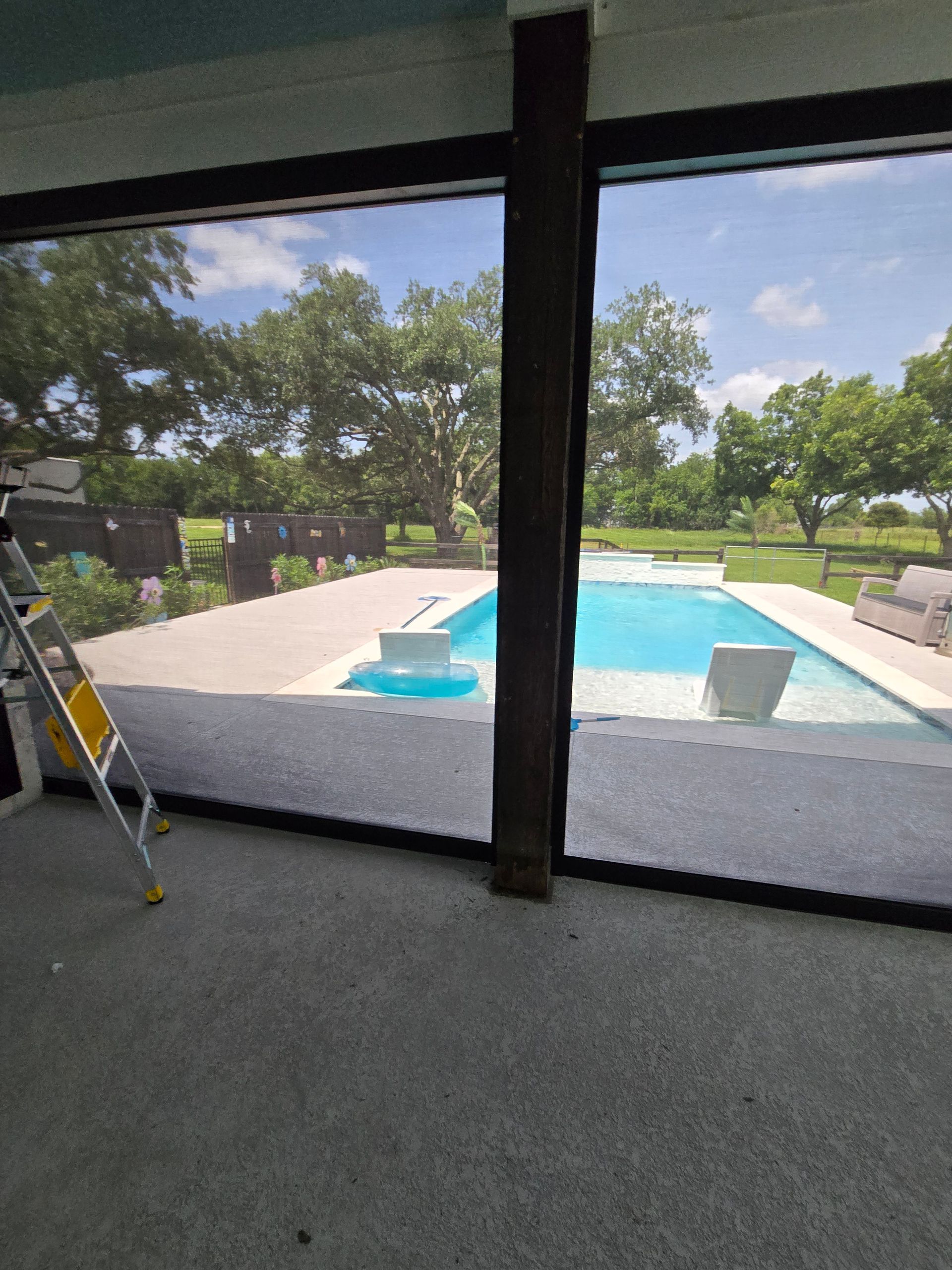 Back patio view of a turquoise swimming pool, green lawn, and trees beyond a screened porch frame