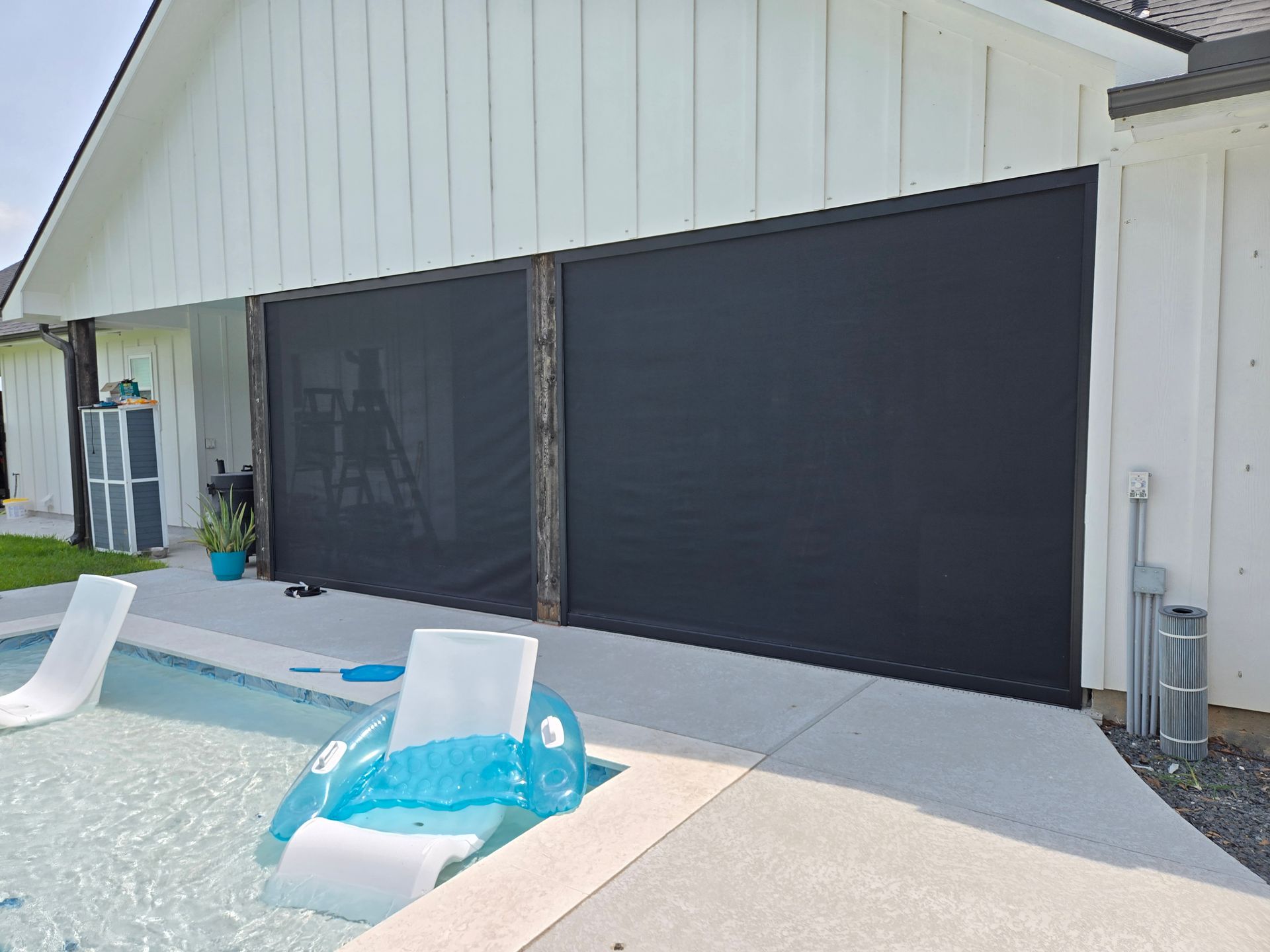 Backyard pool patio with two blue-and-white lounge floats beside a white house and screened porch.