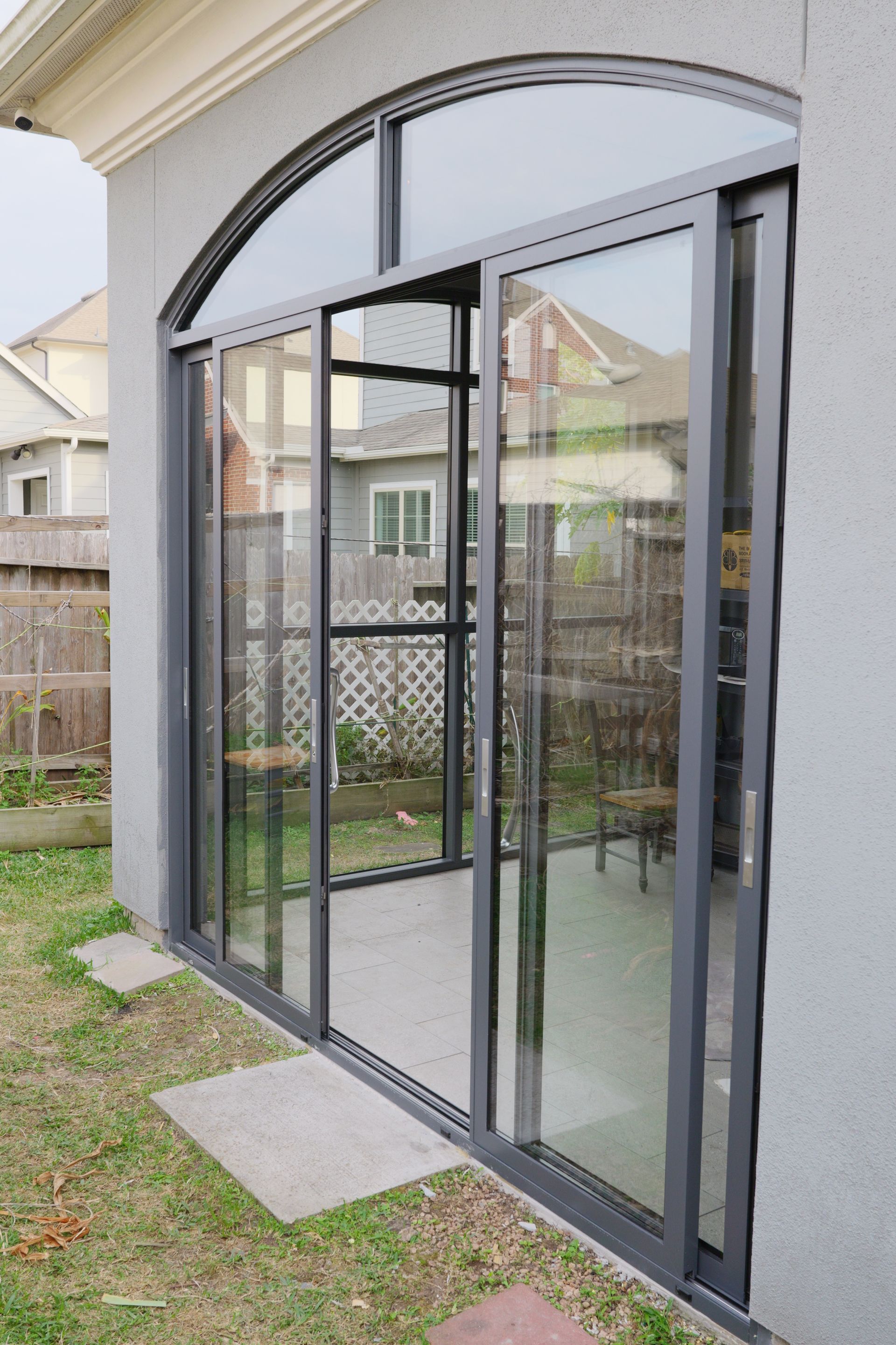 Black-framed glass patio doors under an arched opening beside a backyard lawn
