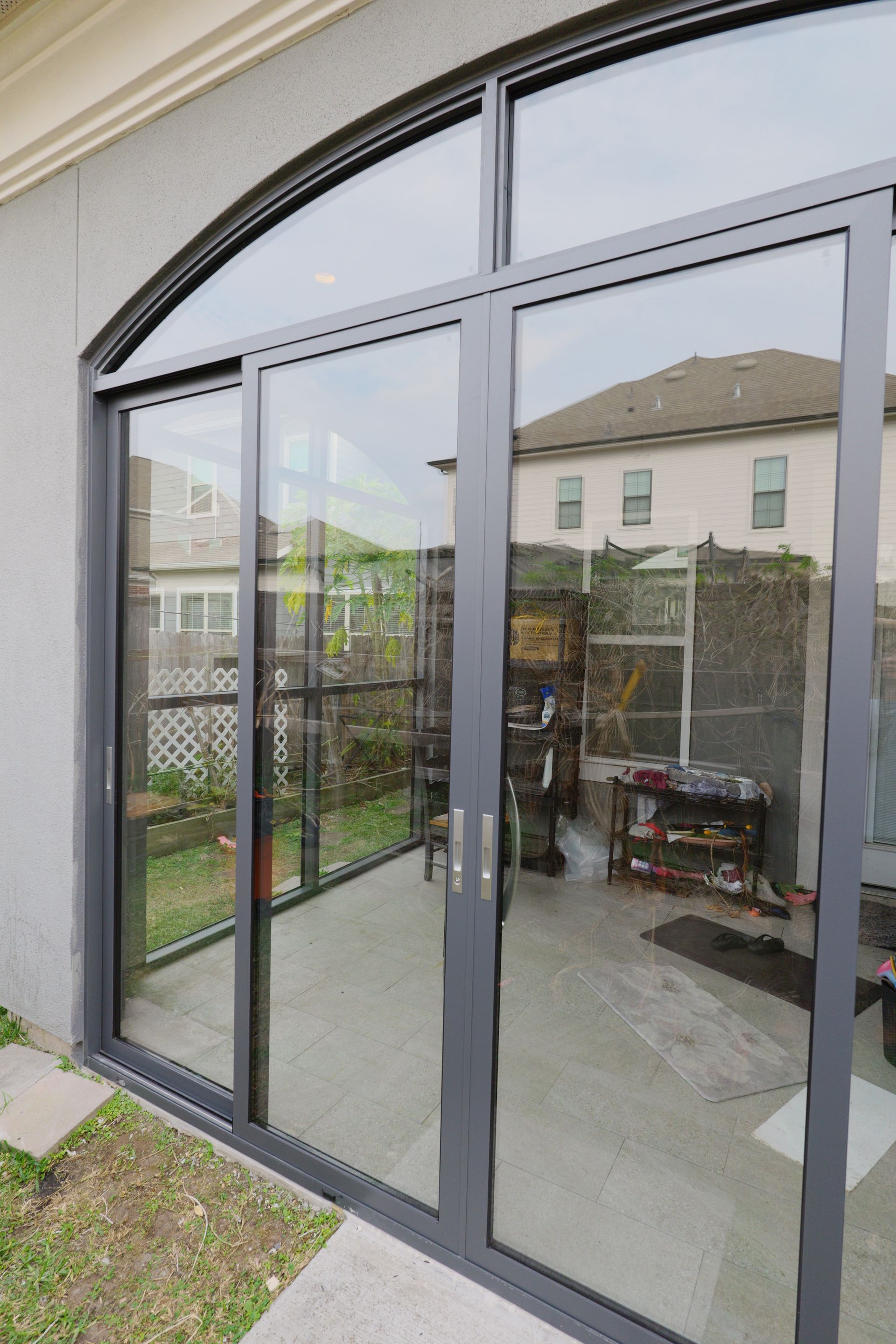 Glass patio doors with black frames reflecting a backyard and neighboring house