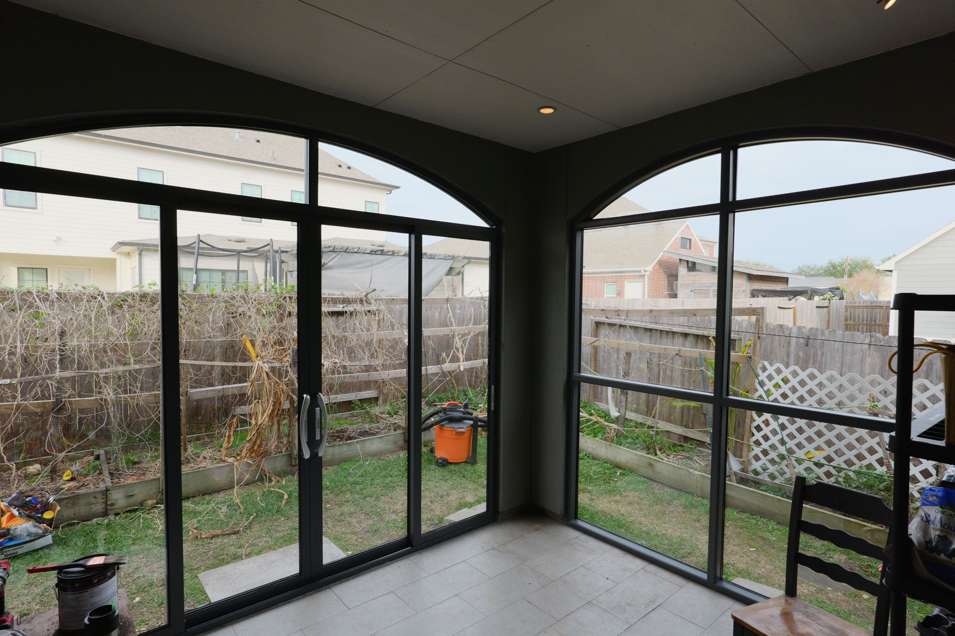Covered patio with black-framed glass doors, tiled floor, and a small fenced backyard.