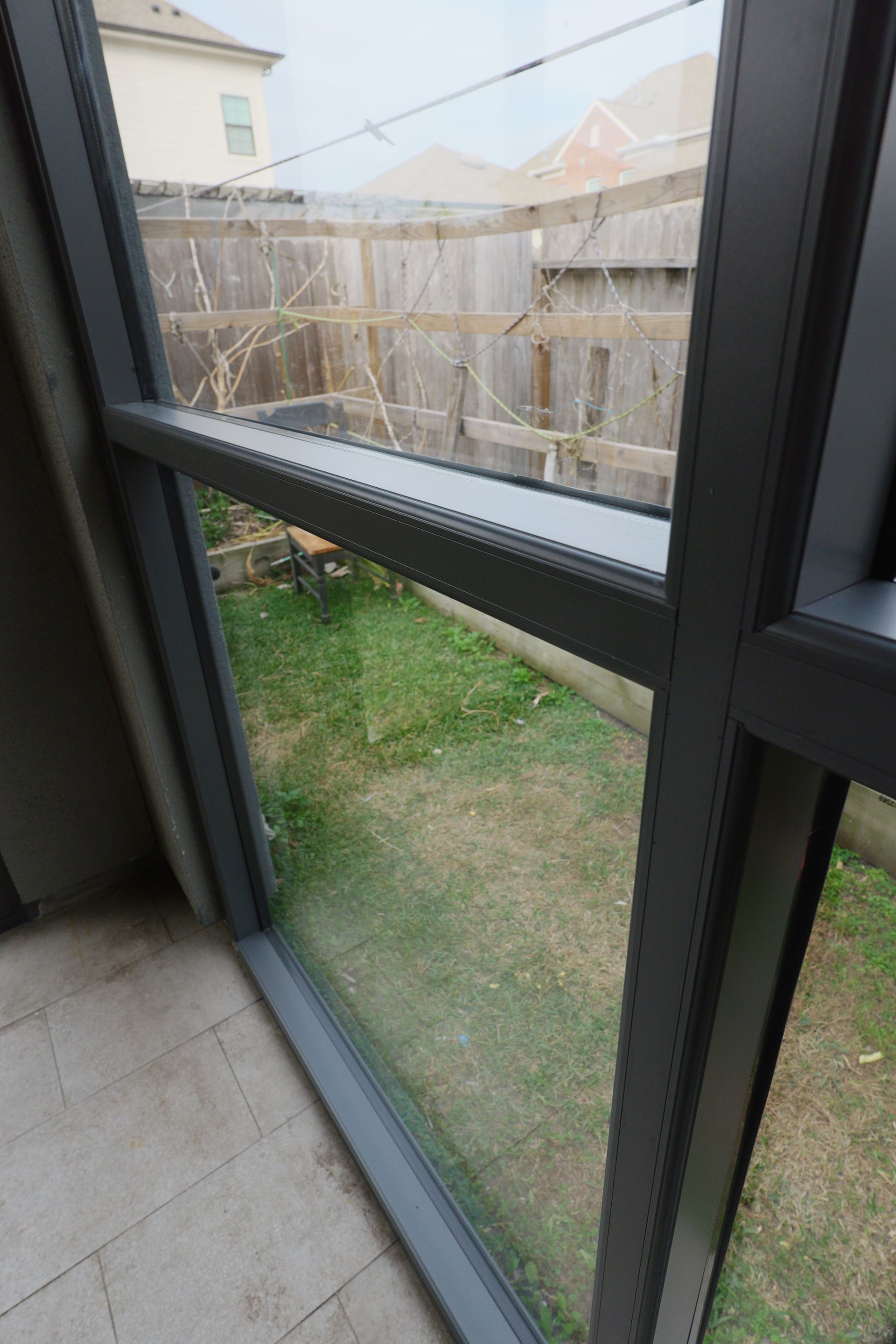 View through a window to a fenced backyard with grass and neighboring houses.
