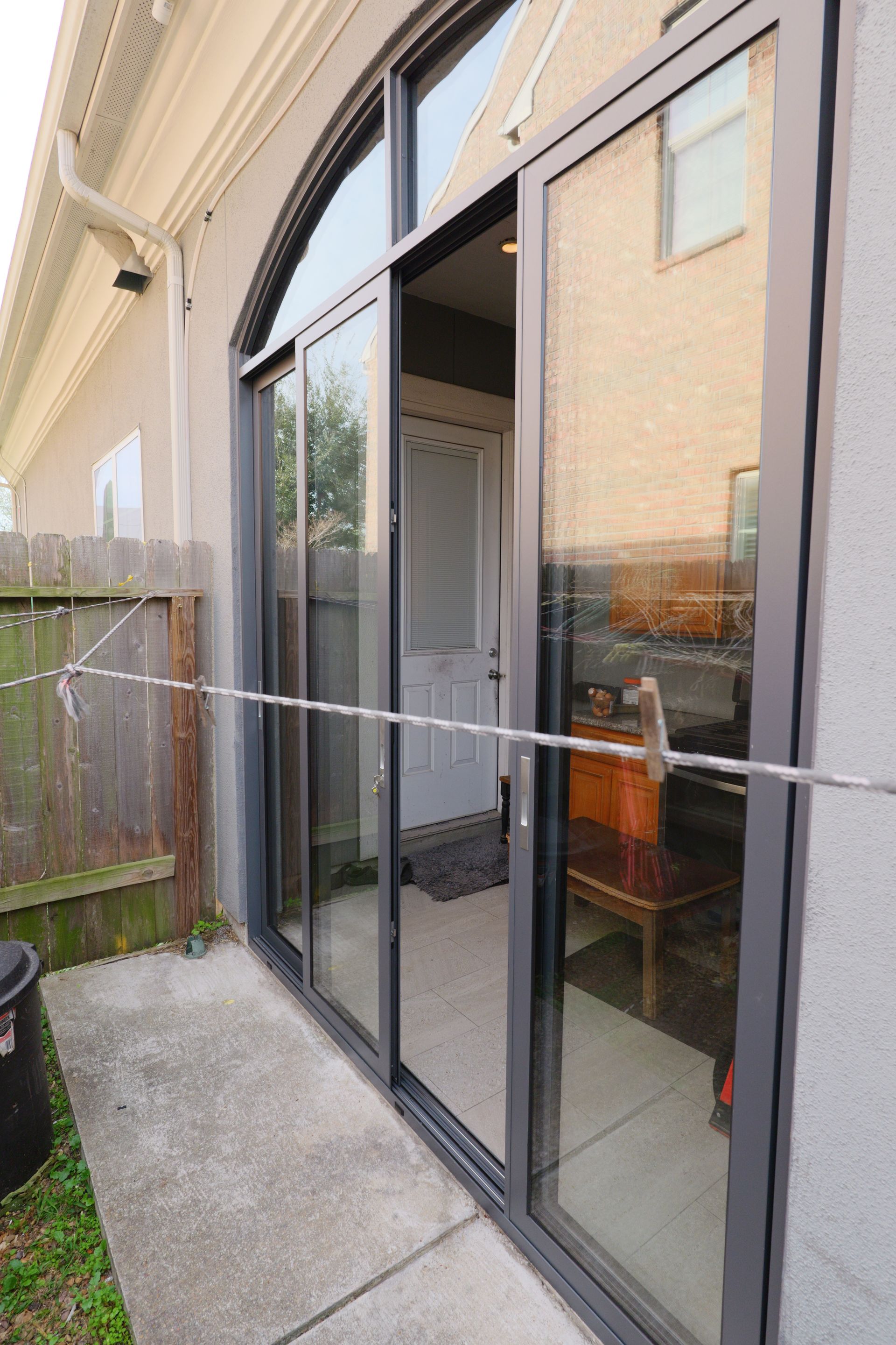 Sliding glass doors to a patio with a chair inside and a wooden fence beside a narrow concrete path