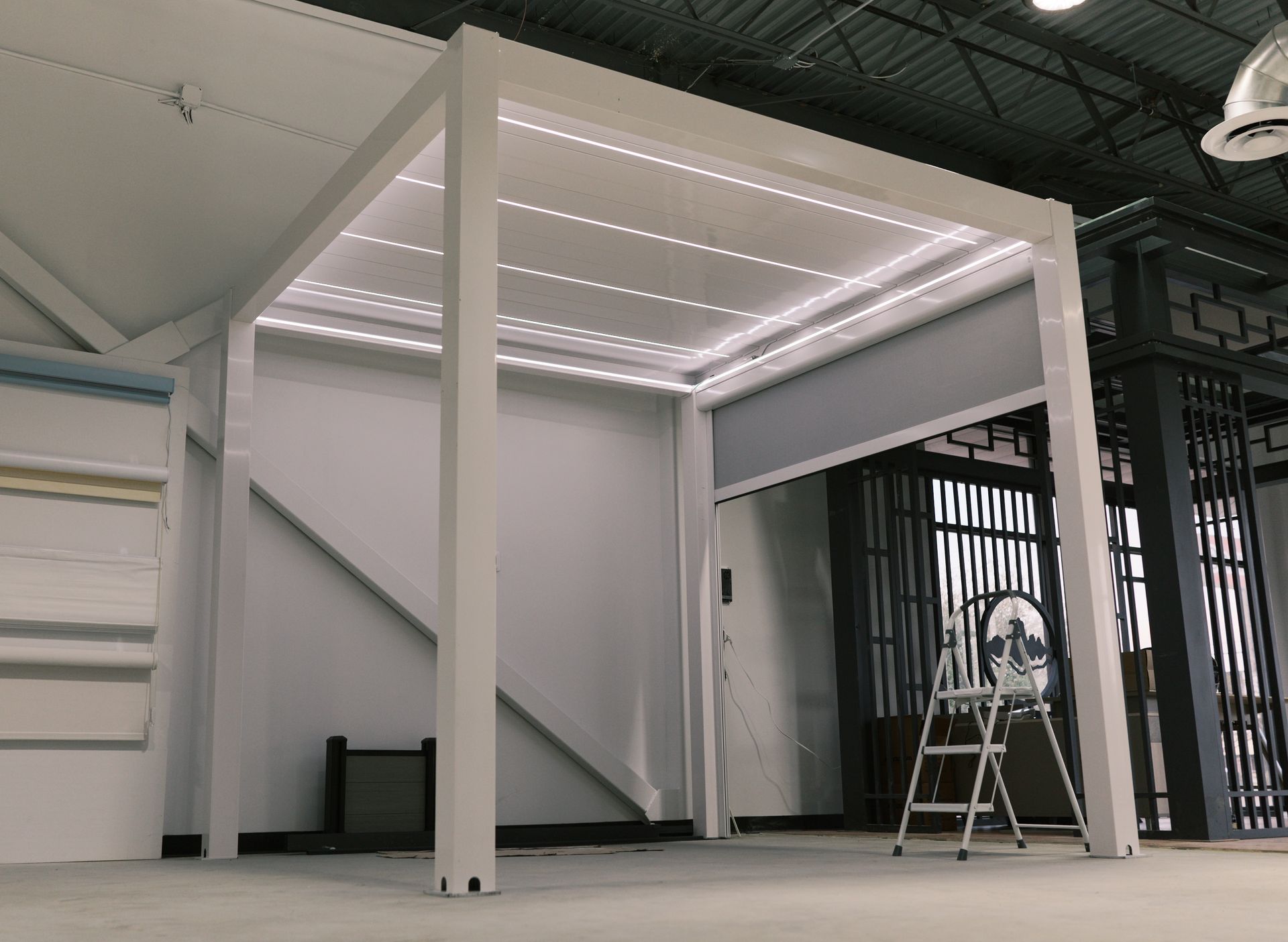 Small white modular structure with LED ceiling lights in an industrial warehouse, with a ladder beside it